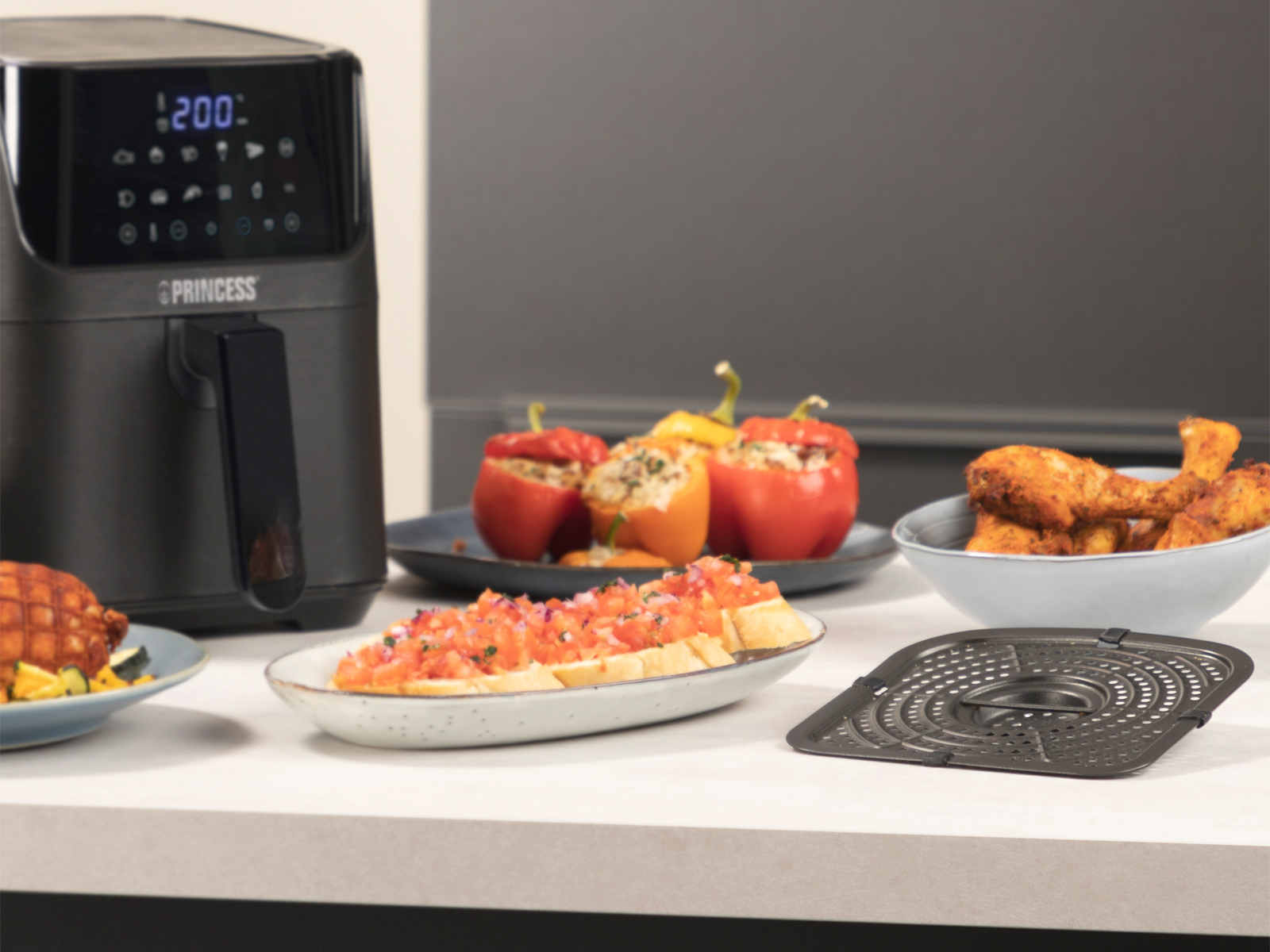 Una freidora de aire con comida cocinada en platos: pimientos rellenos, bruschetta y pollo.