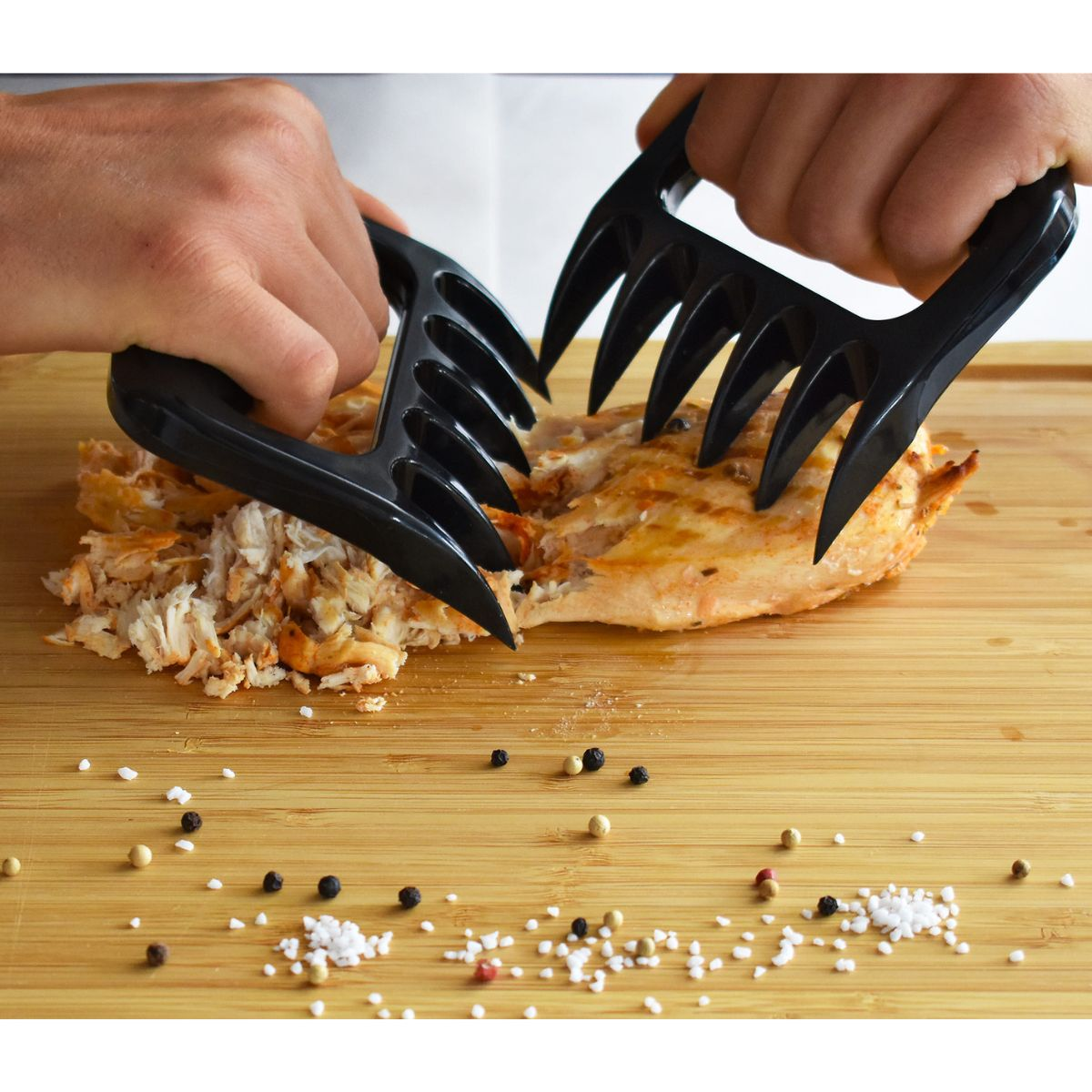 Schwarze Fleischkrallen zerreißen gekochtes Hähnchen auf einem Holzbrett mit Gewürzen.