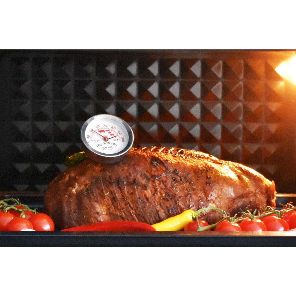 Im Ofen gebackenes Fleisch mit Fleischthermometer. Tomaten und gelber Pfeffer. Schwarzes Backblech.