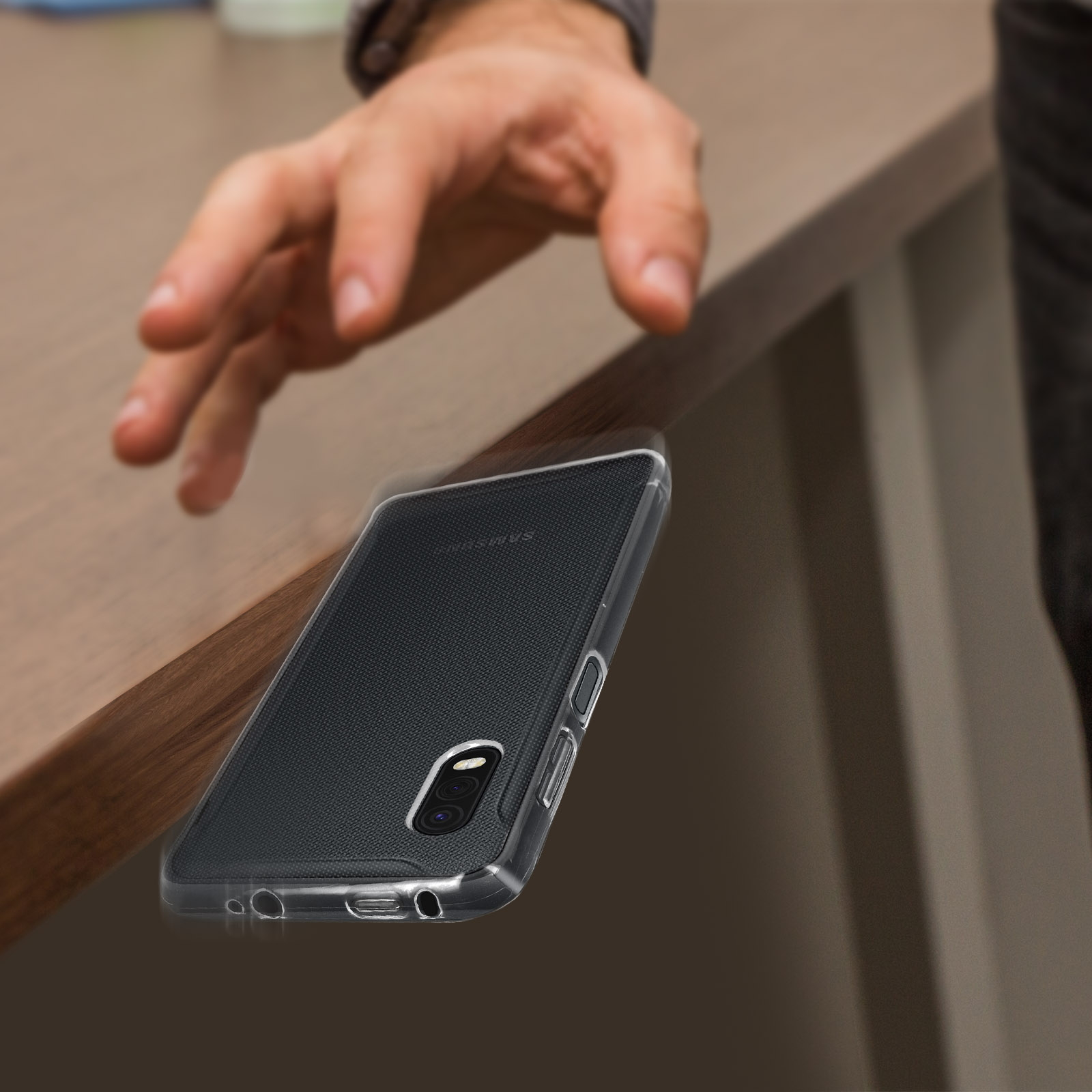 Eine Hand kurz davor, ein Telefon in einer durchsichtigen Hülle auf einen Holztisch fallen zu lassen.
