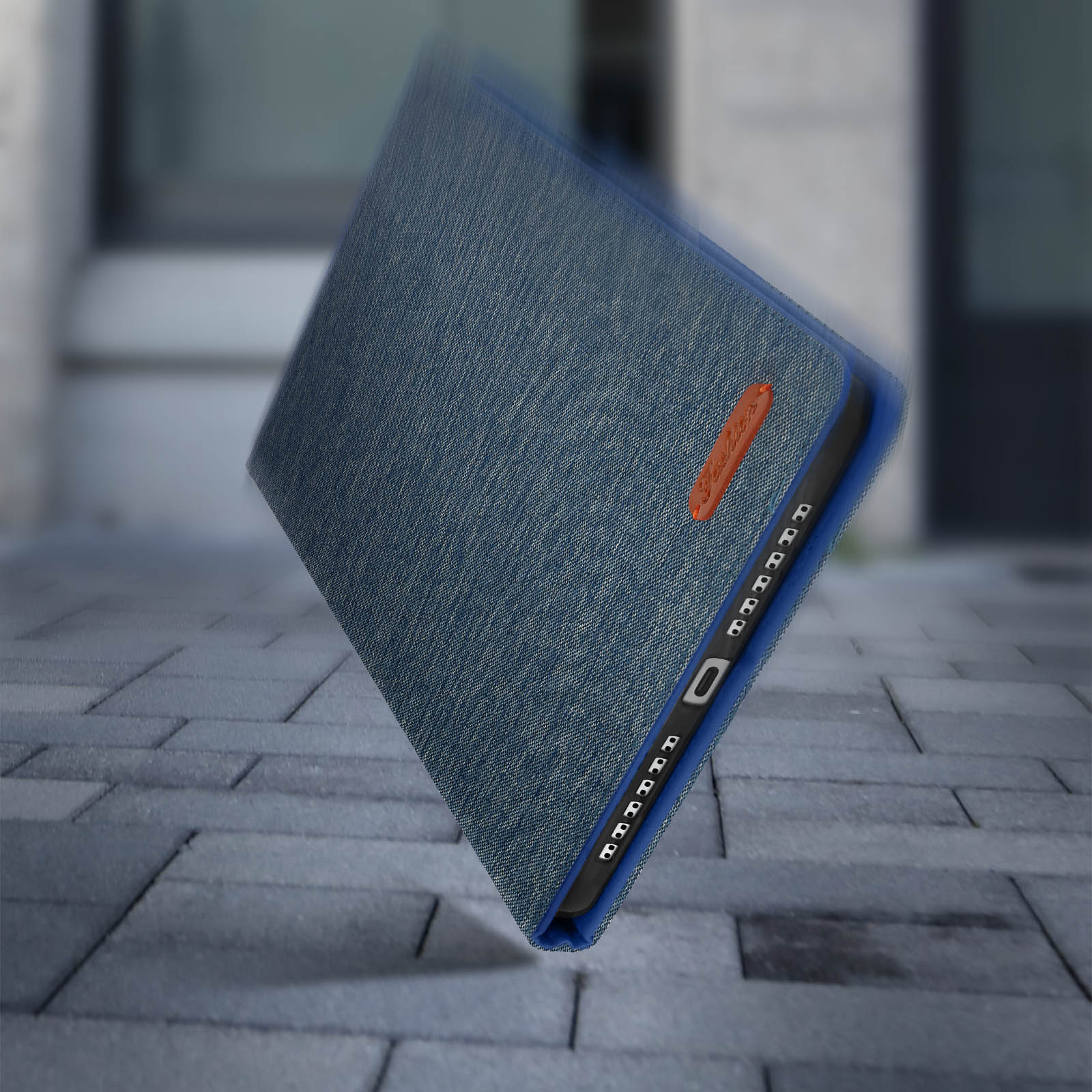 Custodia blu denim, leggermente inclinata, con dettaglio arancione, su pavé.