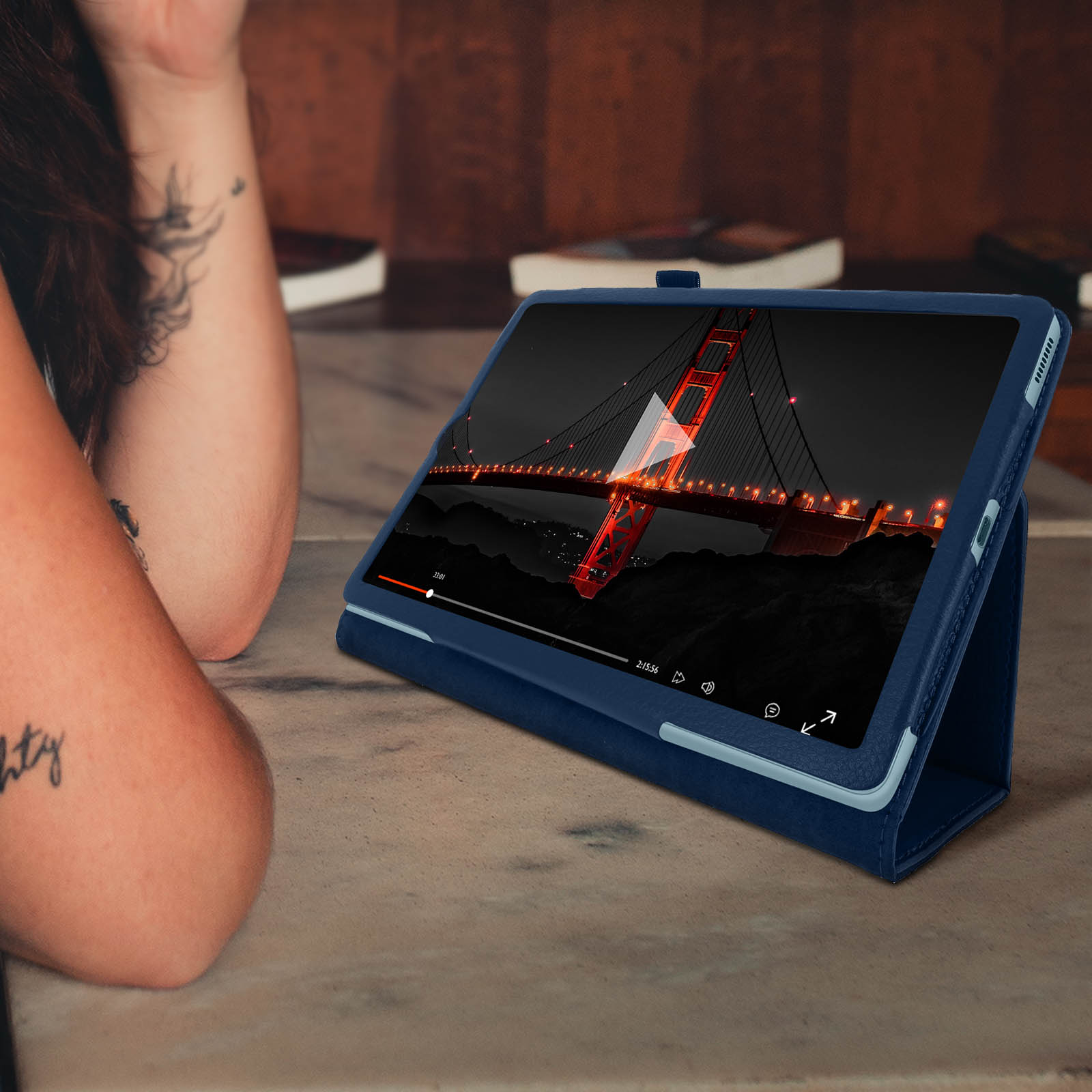 Un tablet che mostra un video di un ponte, appoggiato su una custodia. Il braccio e il tatuaggio di una persona sono nell'inquadratura.