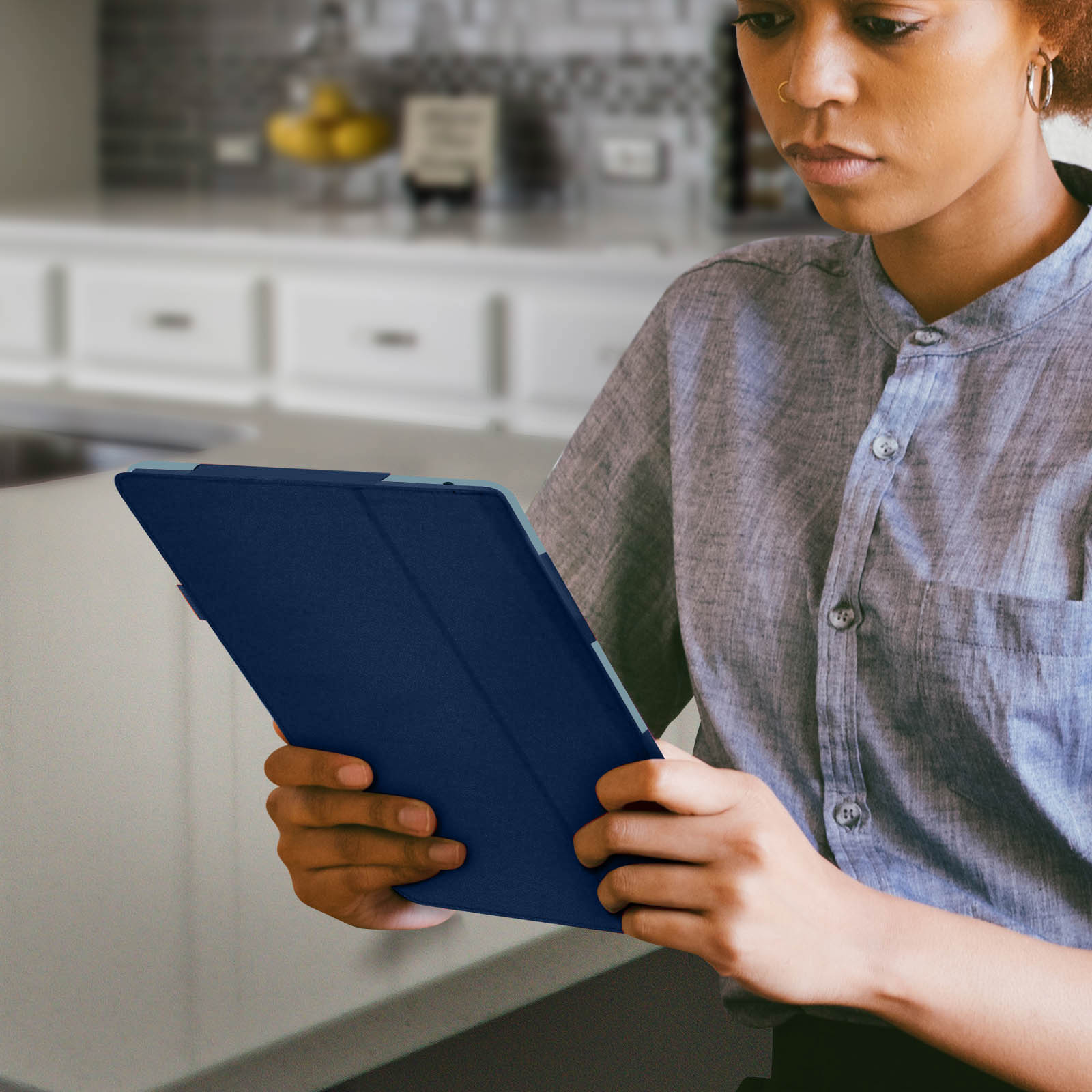 Donna che tiene una custodia per tablet blu, in un ambiente cucina, guardando in basso.