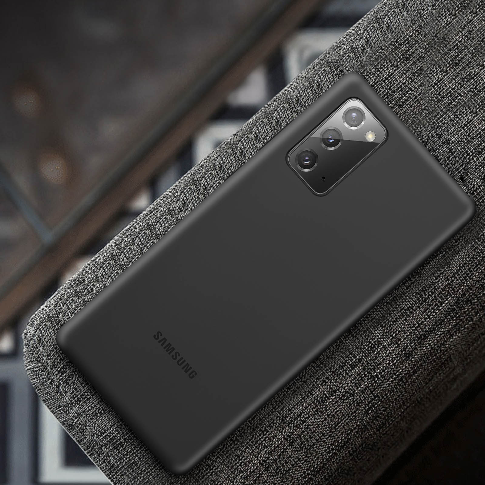 Teléfono negro sobre una superficie gris. El teléfono tiene tres lentes y el logo de Samsung.