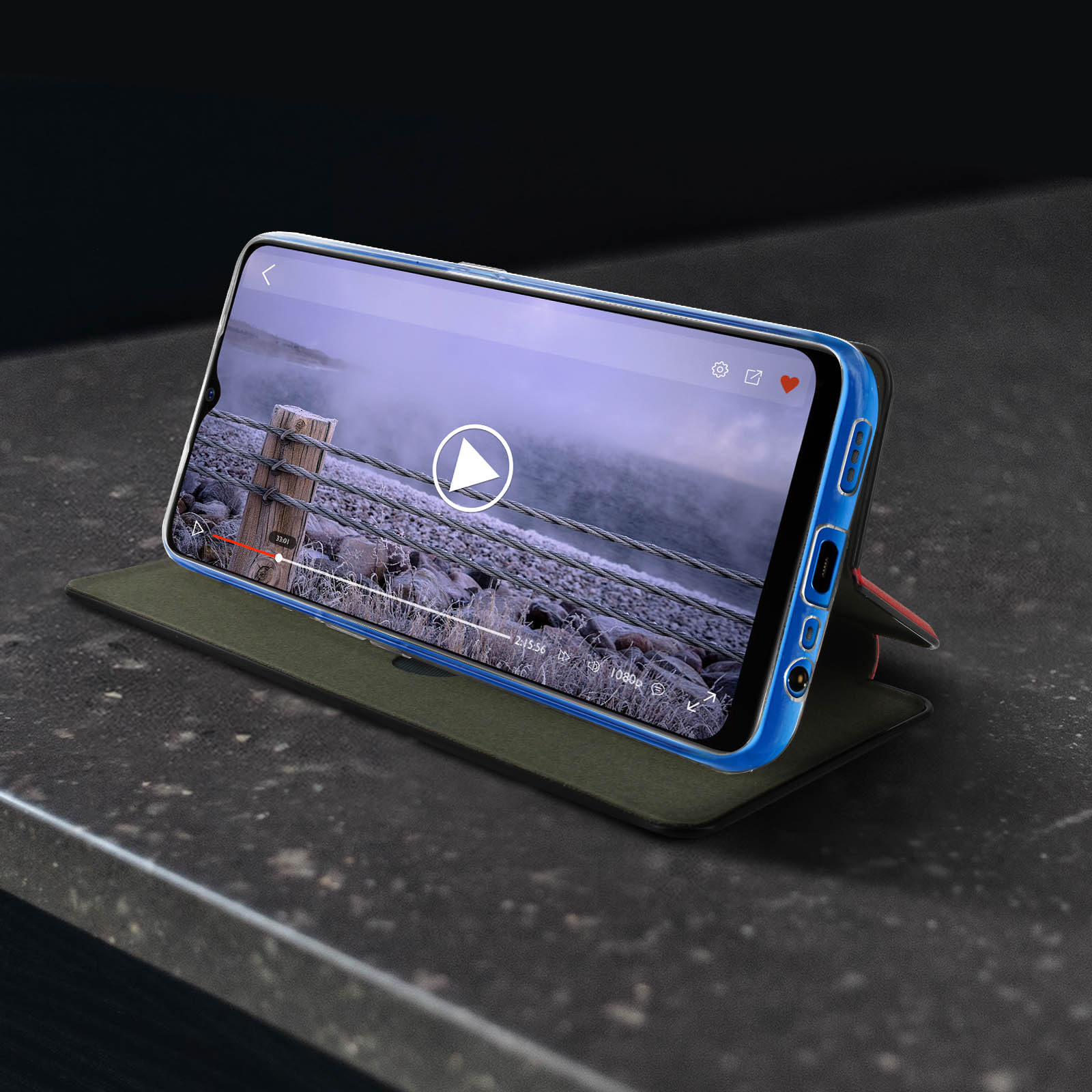 Smartphone in custodia blu mostra video su tavolo. La custodia è su un supporto.