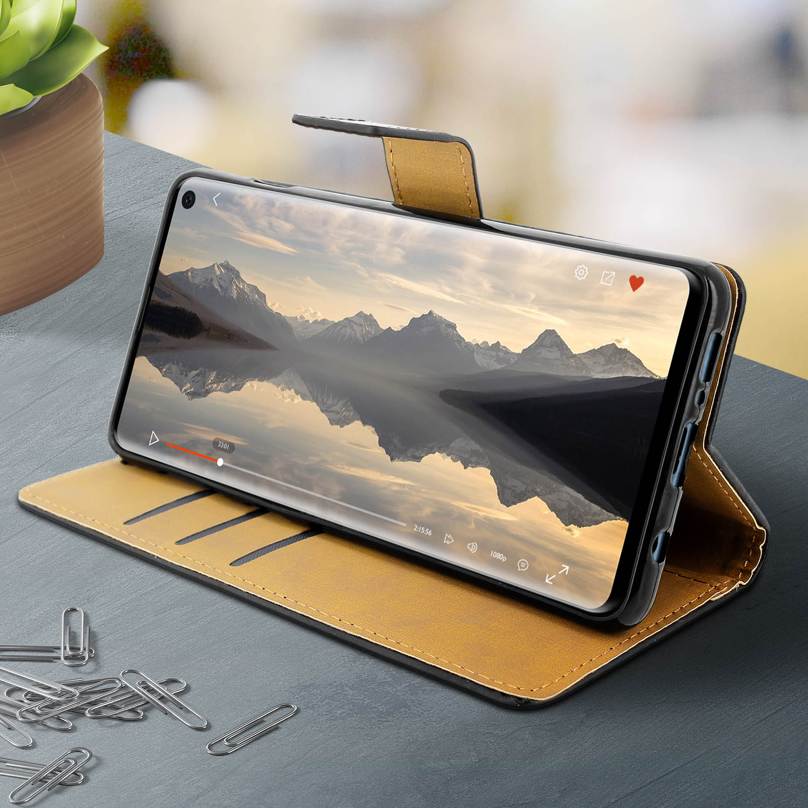Uno smartphone in una custodia marrone che mostra un video con montagne.