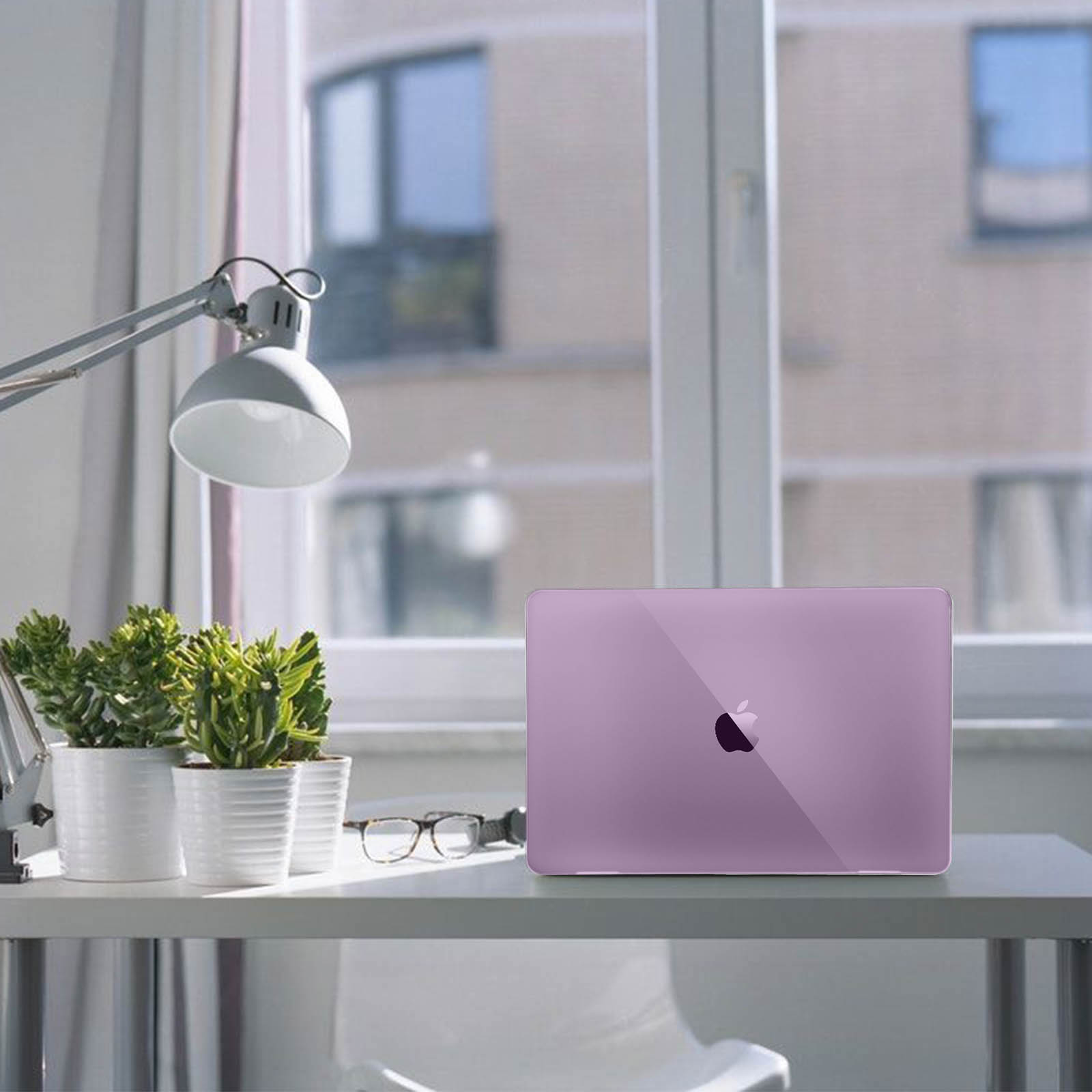 Un ordinateur portable violet sur un bureau blanc. Il y a des plantes, des lunettes et une lampe.