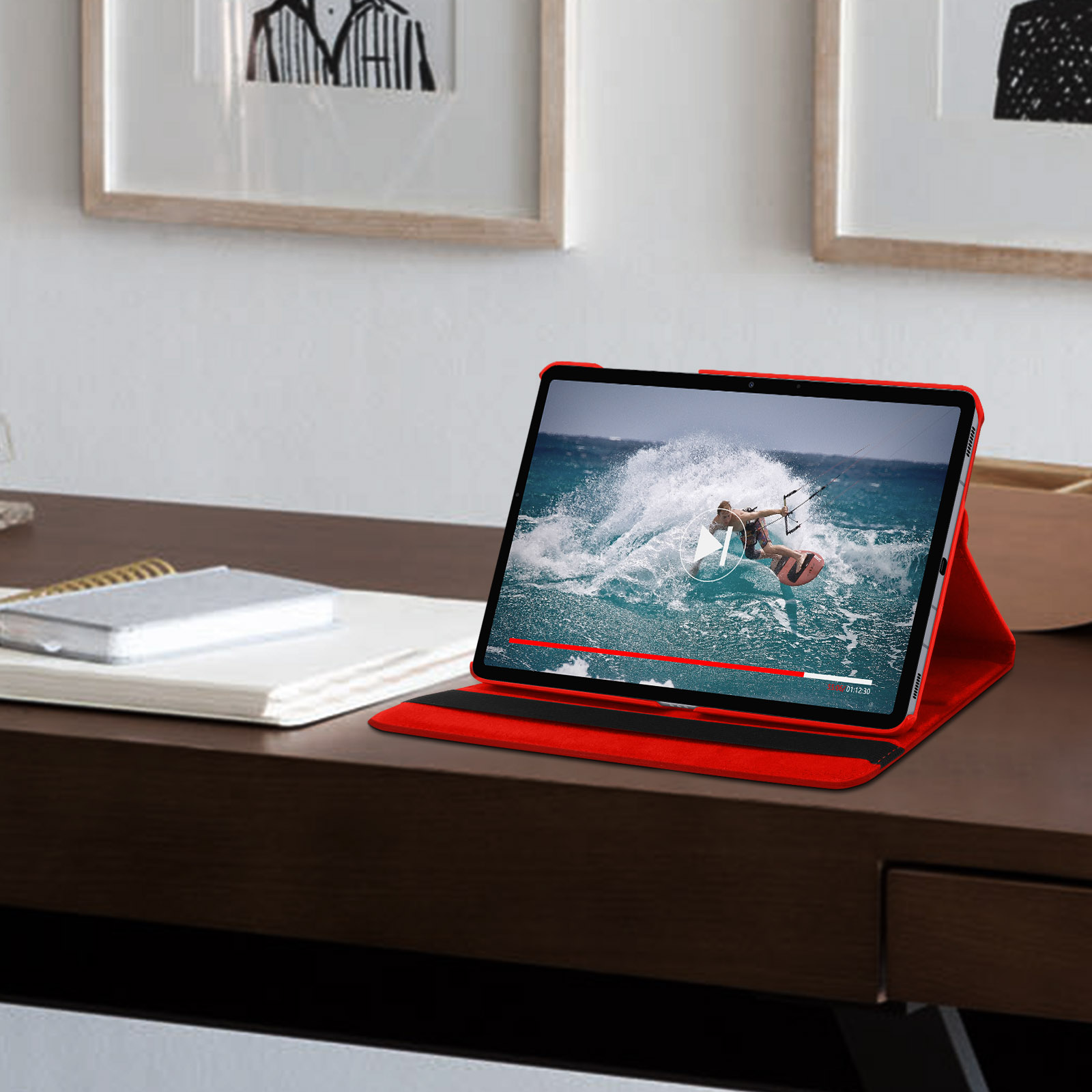 Un tablet in custodia rossa mostra un video di un surfista. Sul tavolo, con arte sul muro.