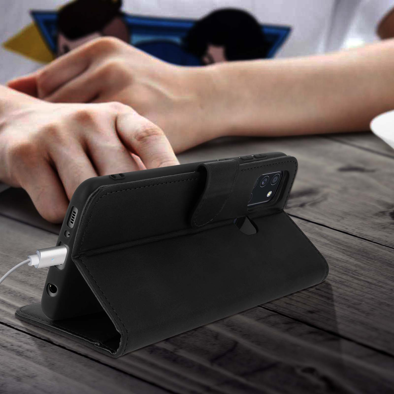 Een telefoon in een zwarte hoes op een houten tafel. Een witte oplaadkabel is aangesloten op de telefoon.