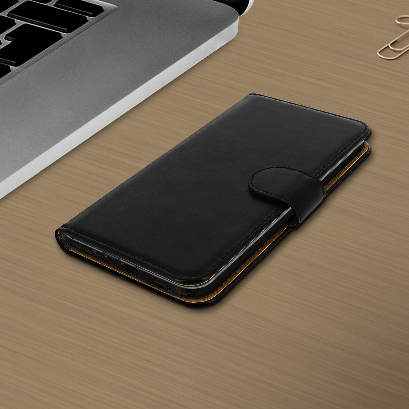 Custodia nera per telefono su un tavolo di legno vicino a un laptop e una graffetta.