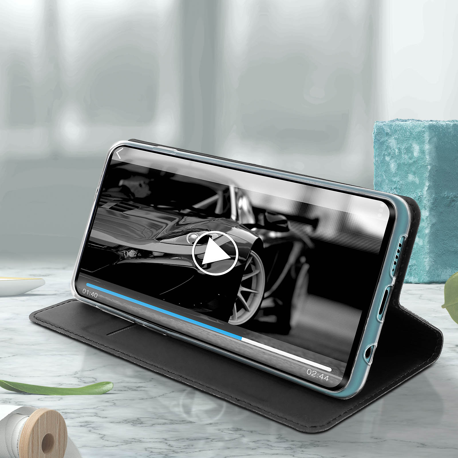 Telefono all'interno di una custodia nera. Riproduce un video. Lo sfondo è un tavolo di marmo con un blocco blu.