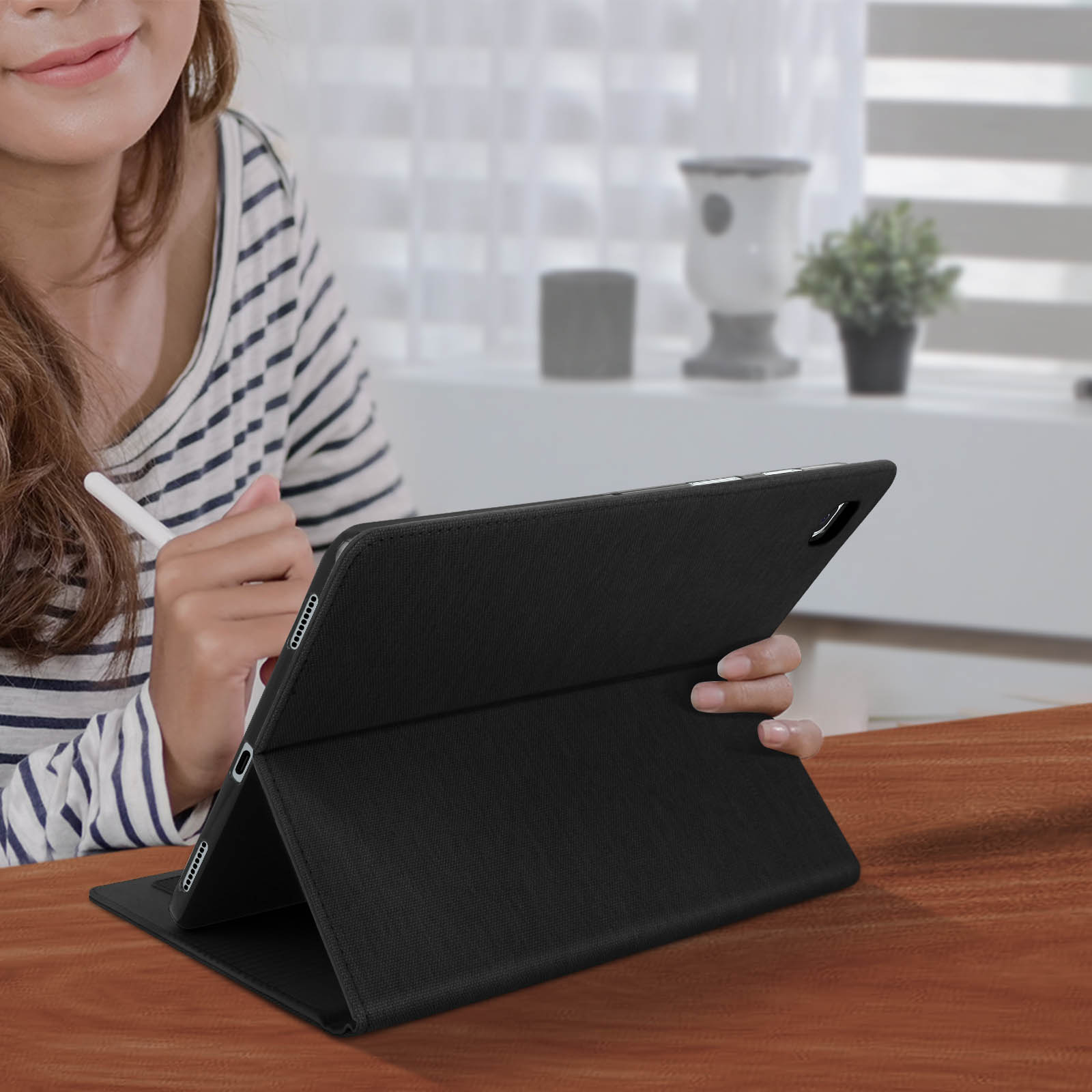 Una donna tiene una penna, usando un tablet in una custodia nera. Tavolo di legno marrone.