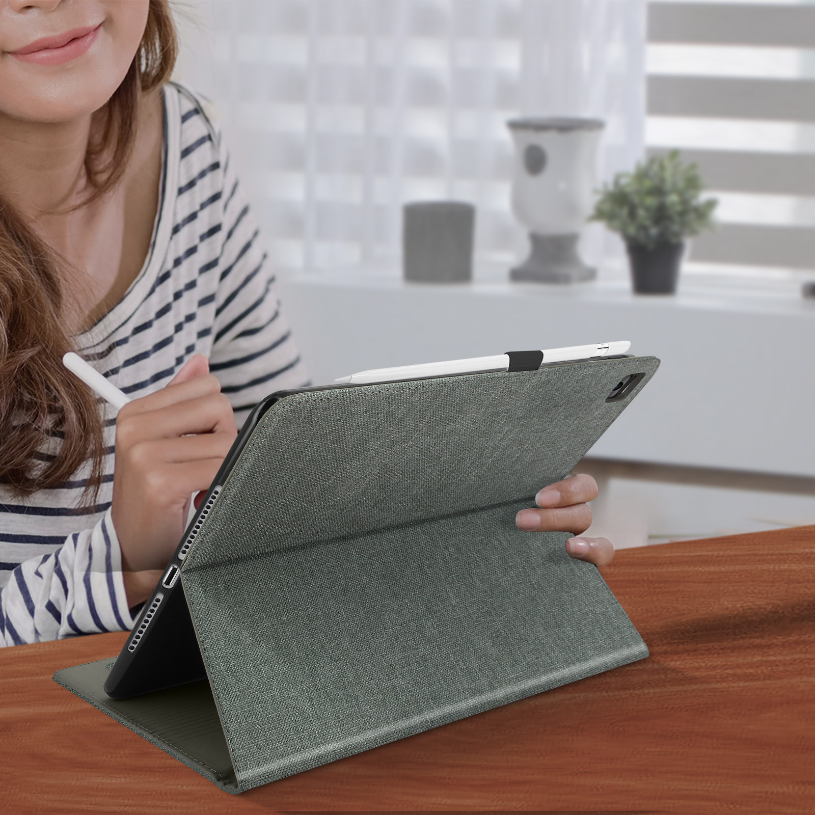 Una donna usa un tablet con una matita. Il tablet ha una custodia in tessuto verde. Tavolo di legno.