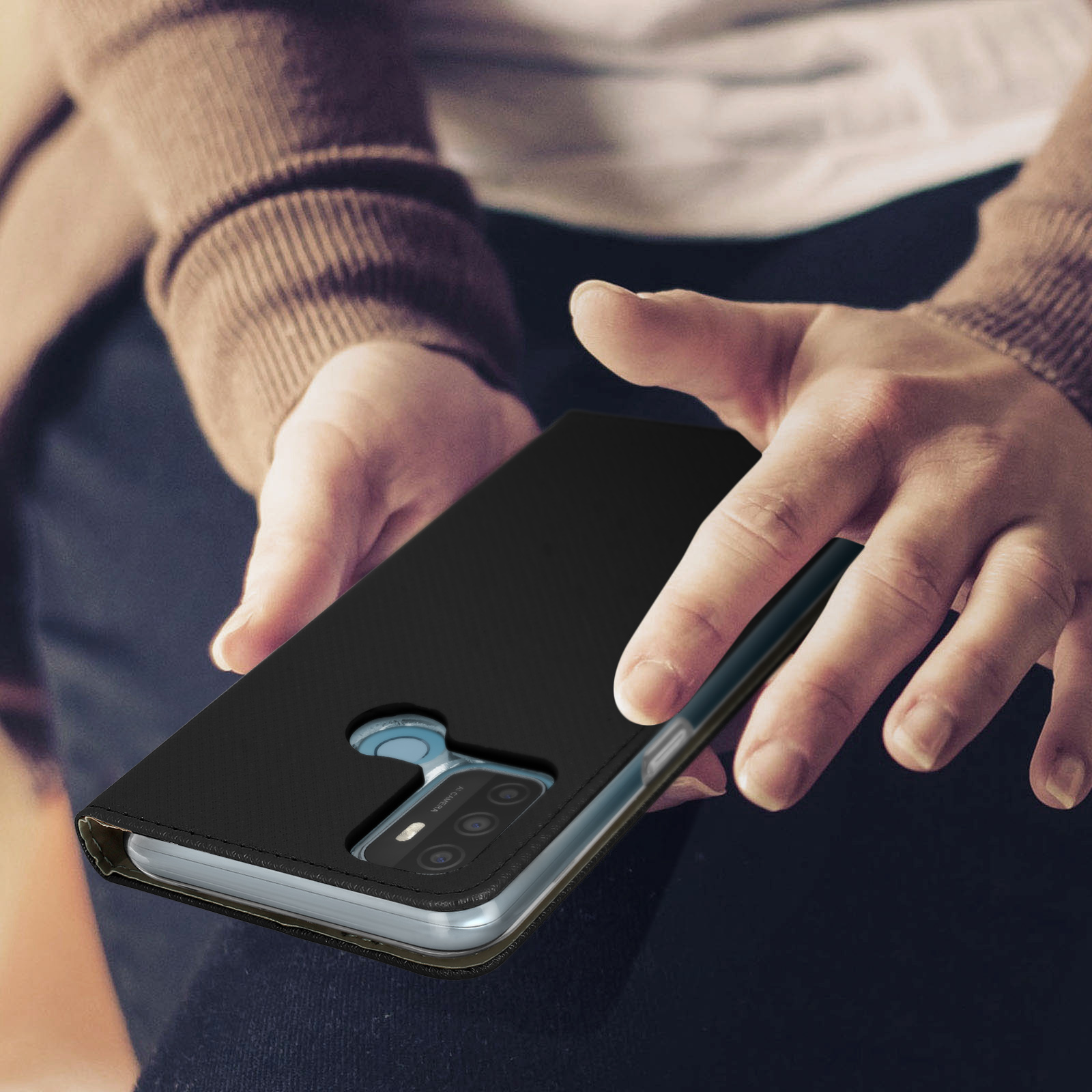 Custodia nera con telefono dentro, tenuta da mani. Sfondo: persona con maglione marrone.