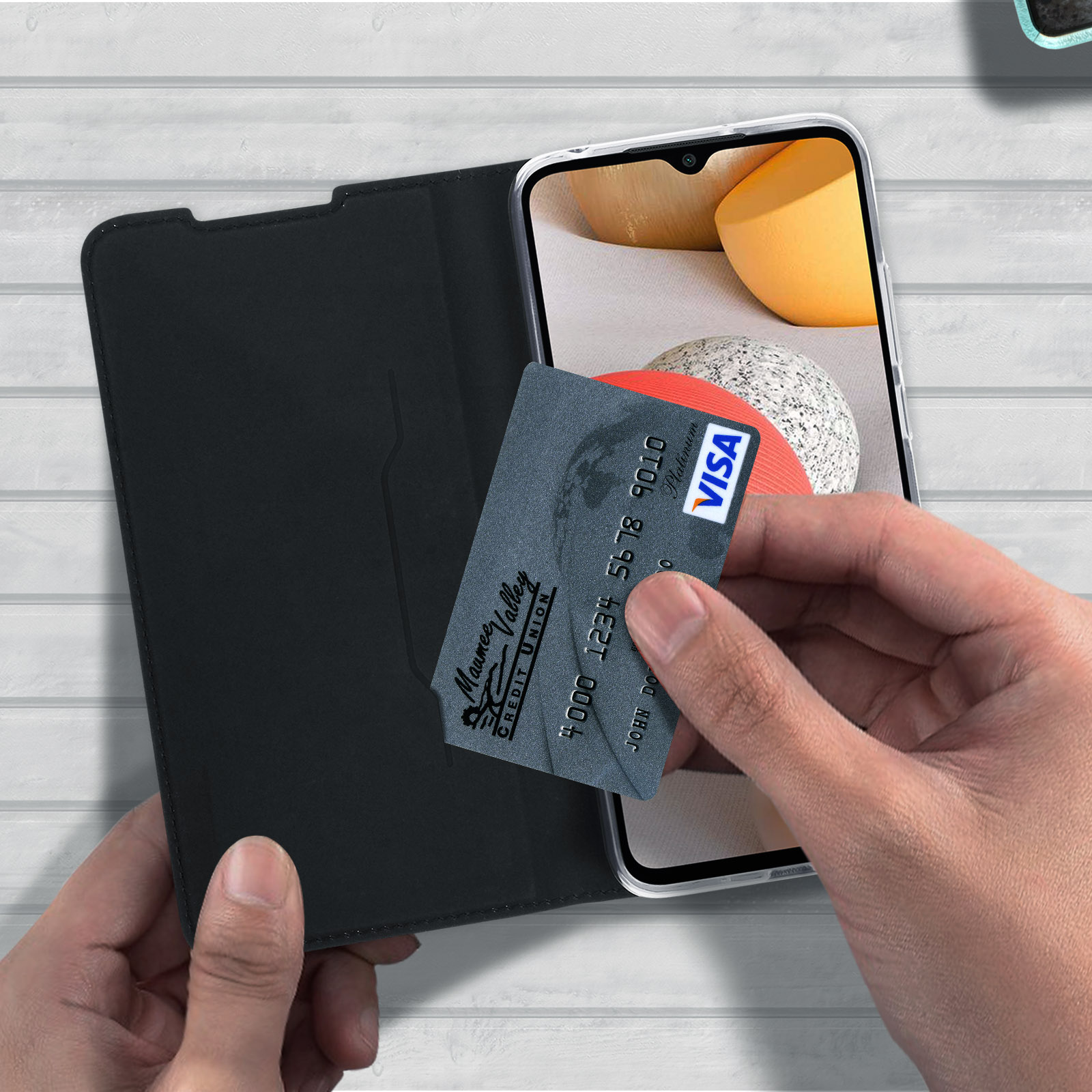 Una persona che tiene un telefono dentro una custodia nera e una carta di credito con logo Visa.