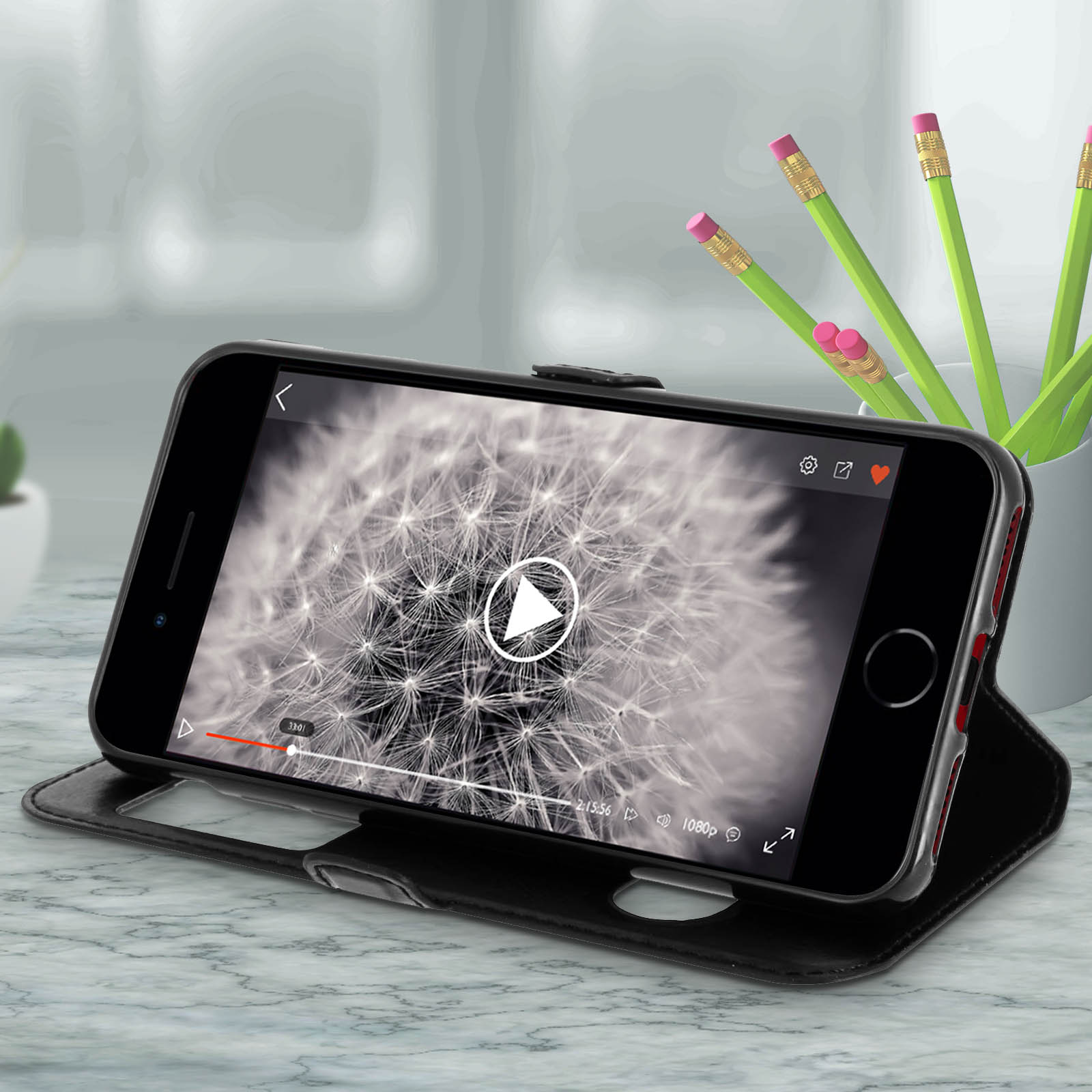 Telefono in custodia nera che mostra un video. Matite in un supporto a destra.