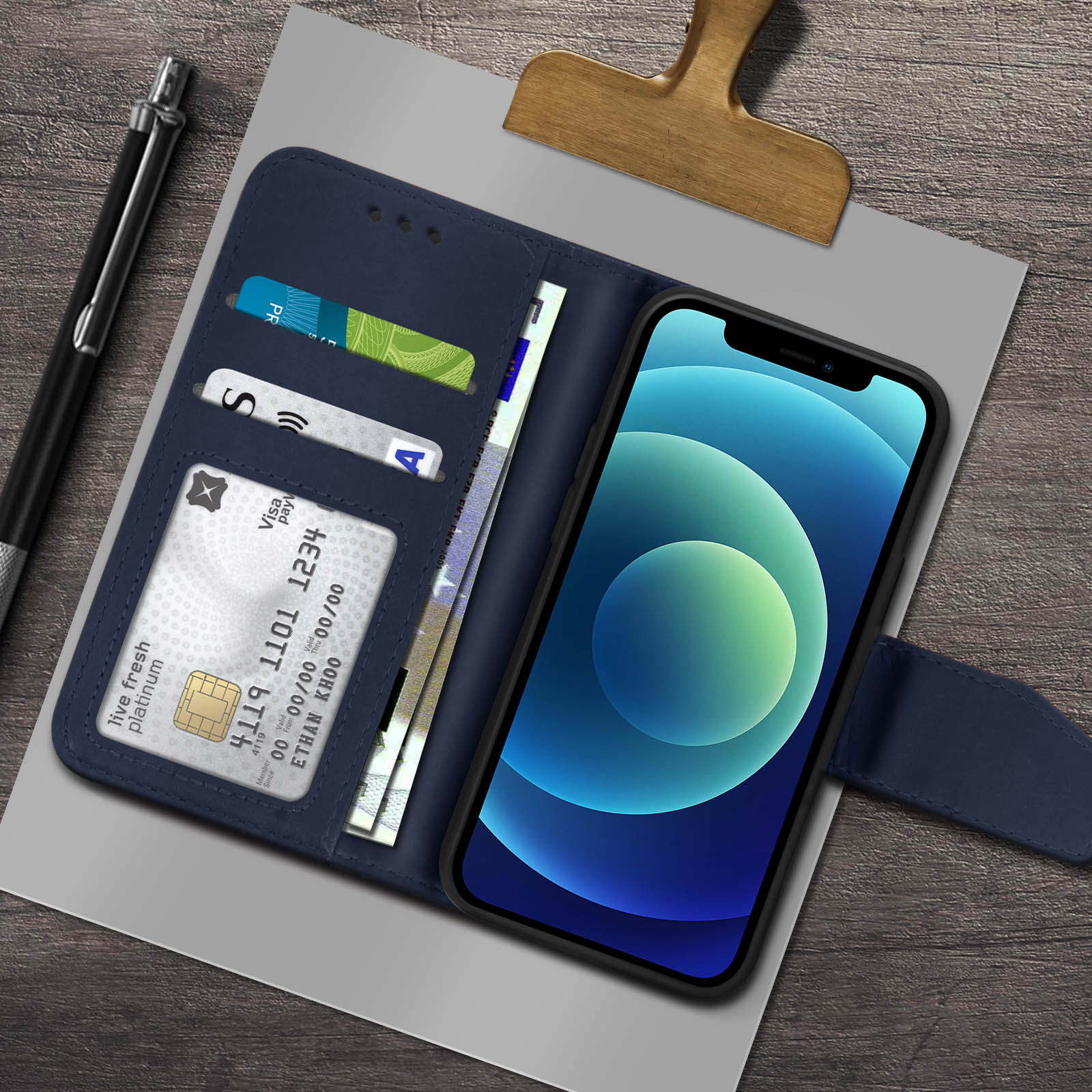 Custodia a portafoglio blu aperta, con telefono, carte e contanti su legno. C'è una penna.