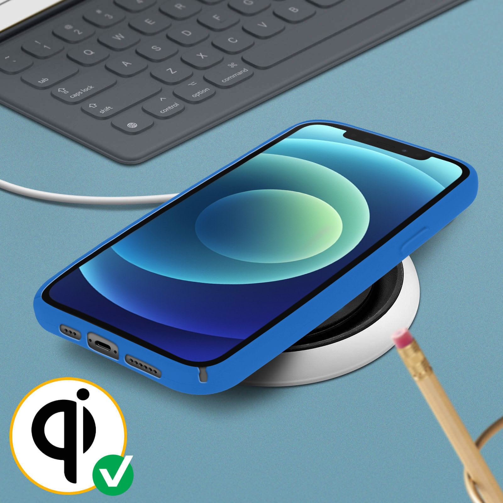 Een telefoon in een blauwe hoes op een draadloze oplader, met een toetsenbord en potlood op de achtergrond.