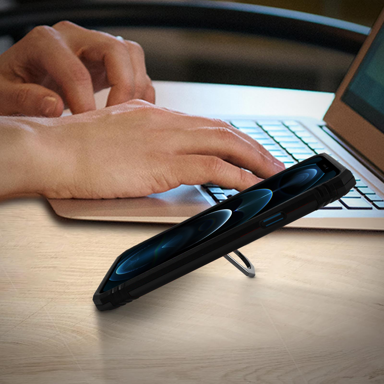 Un telefono con custodia è su un tavolo di legno con un laptop sullo sfondo. Il telefono ha un supporto.