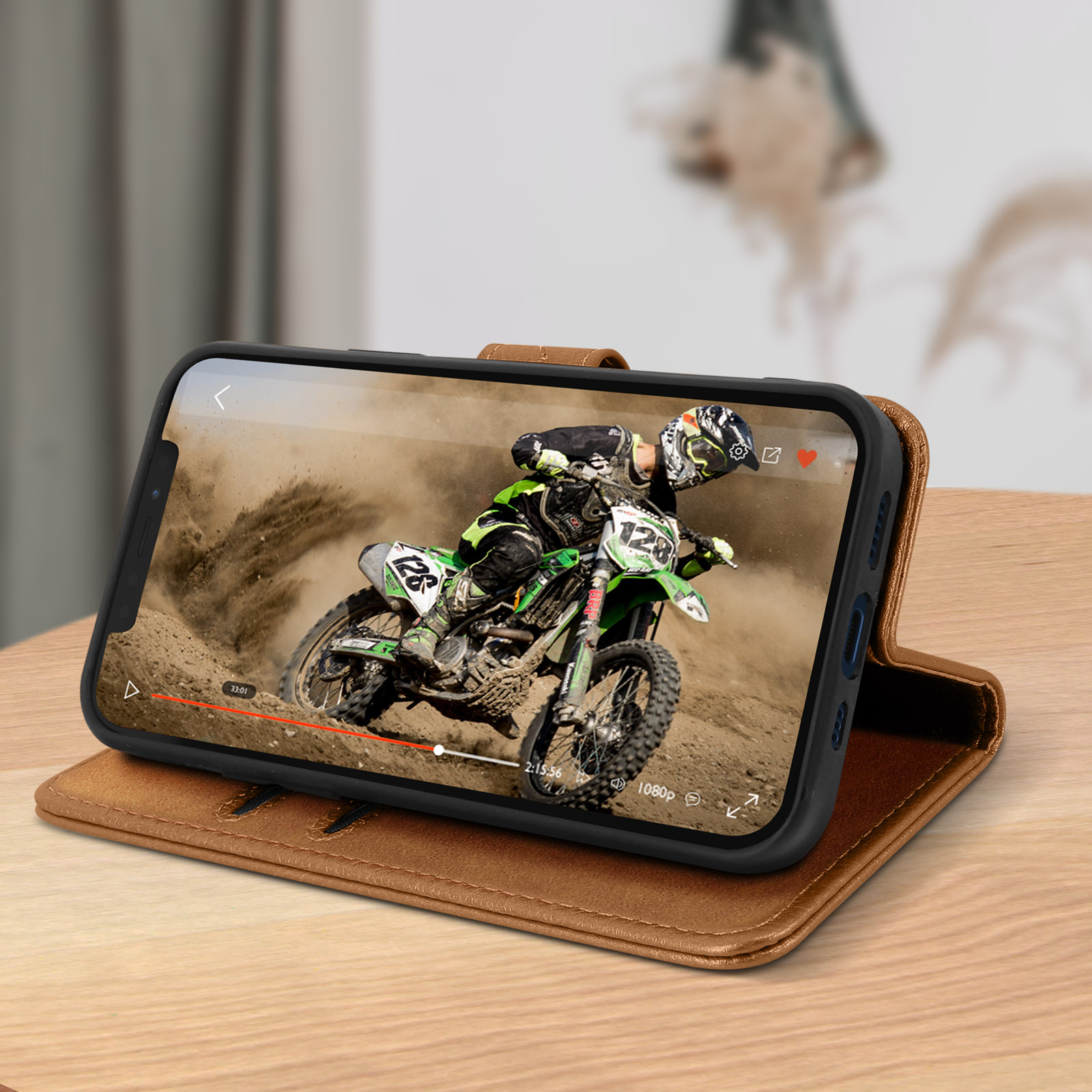 Un téléphone affiche une vidéo de motocross, dans un étui en cuir marron, sur une surface en bois.