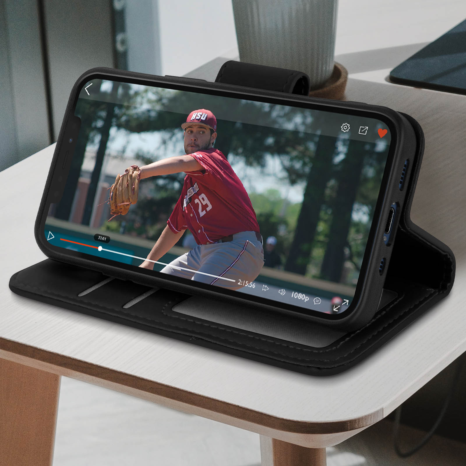 Il telefono in una custodia nera mostra una partita di baseball. Poggia su una custodia a portafoglio nera aperta su un tavolo di legno.