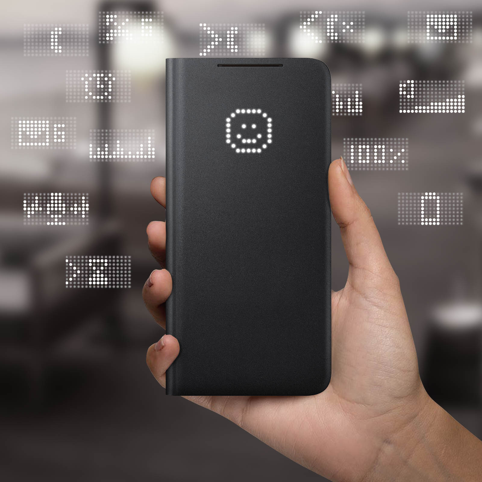Una mano che tiene un telefono nero con una faccina sullo schermo. Lo sfondo è sfocato.