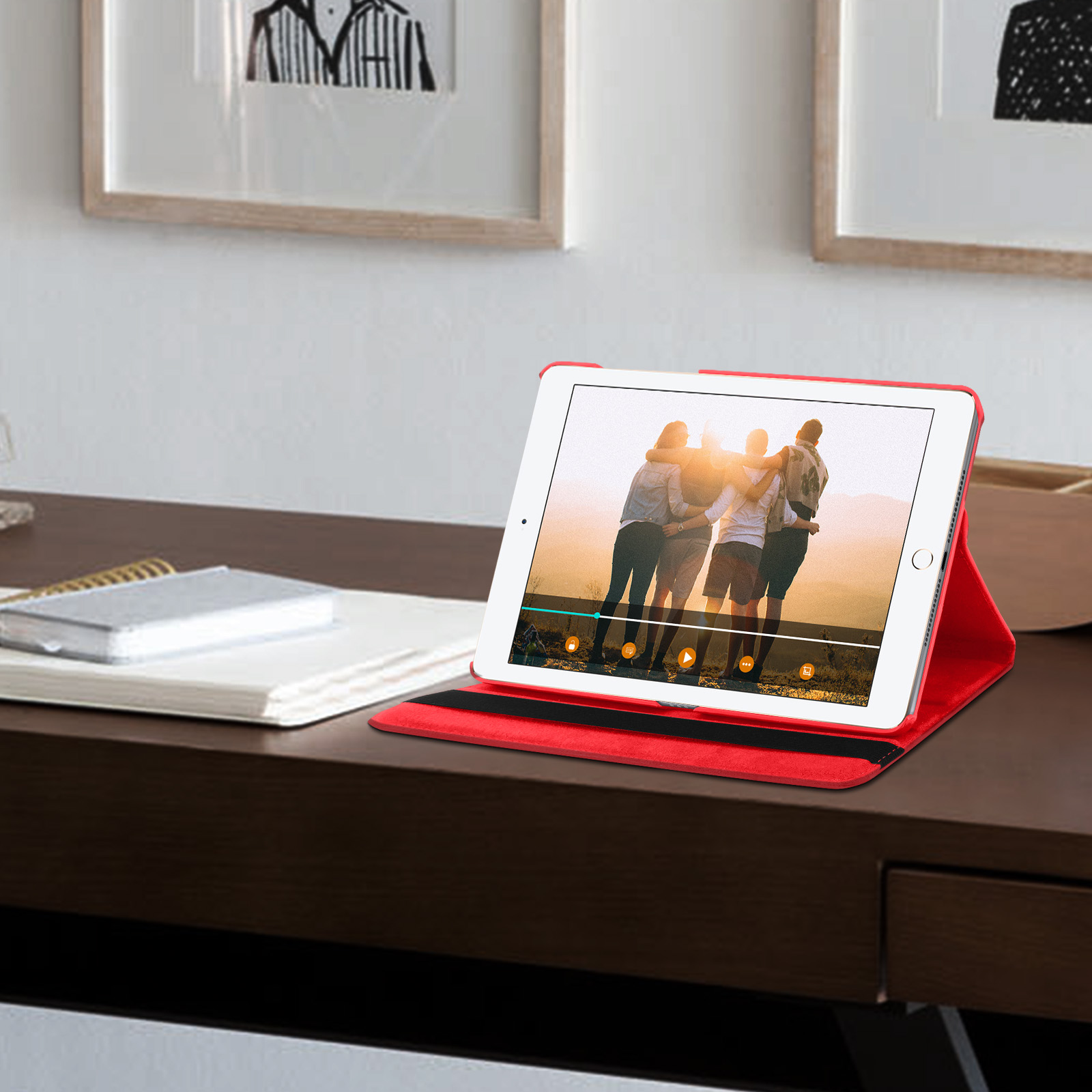 Un iPad mostra un video di persone che si abbracciano. È in un supporto rosso su una scrivania con un blocco.