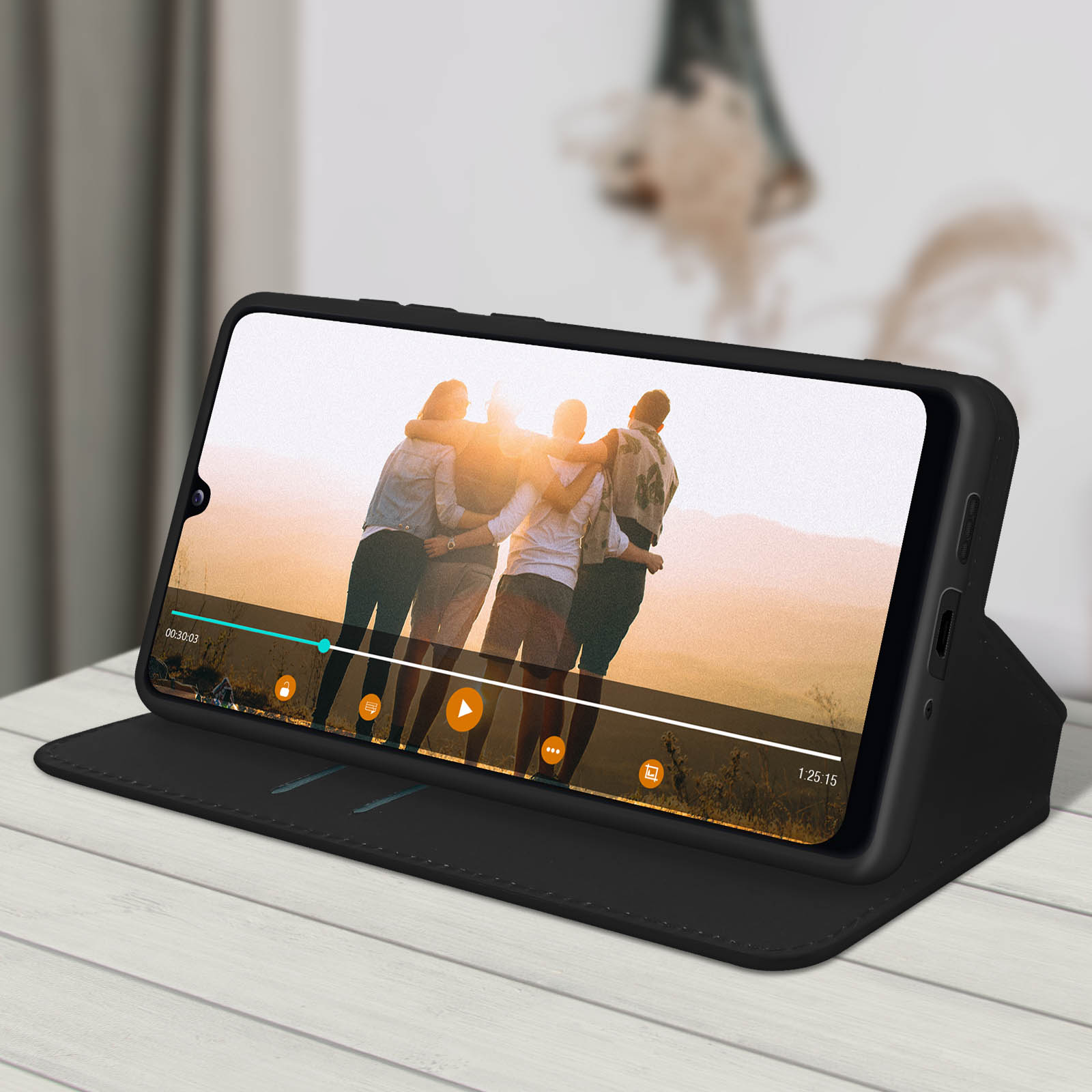 Een telefoon in een zwarte hoes toont een video. De telefoon staat open op een tafel.