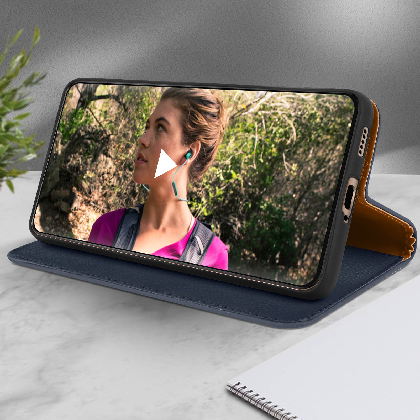 Una donna guarda un video su un telefono con una custodia aperta. La custodia è blu e marrone.