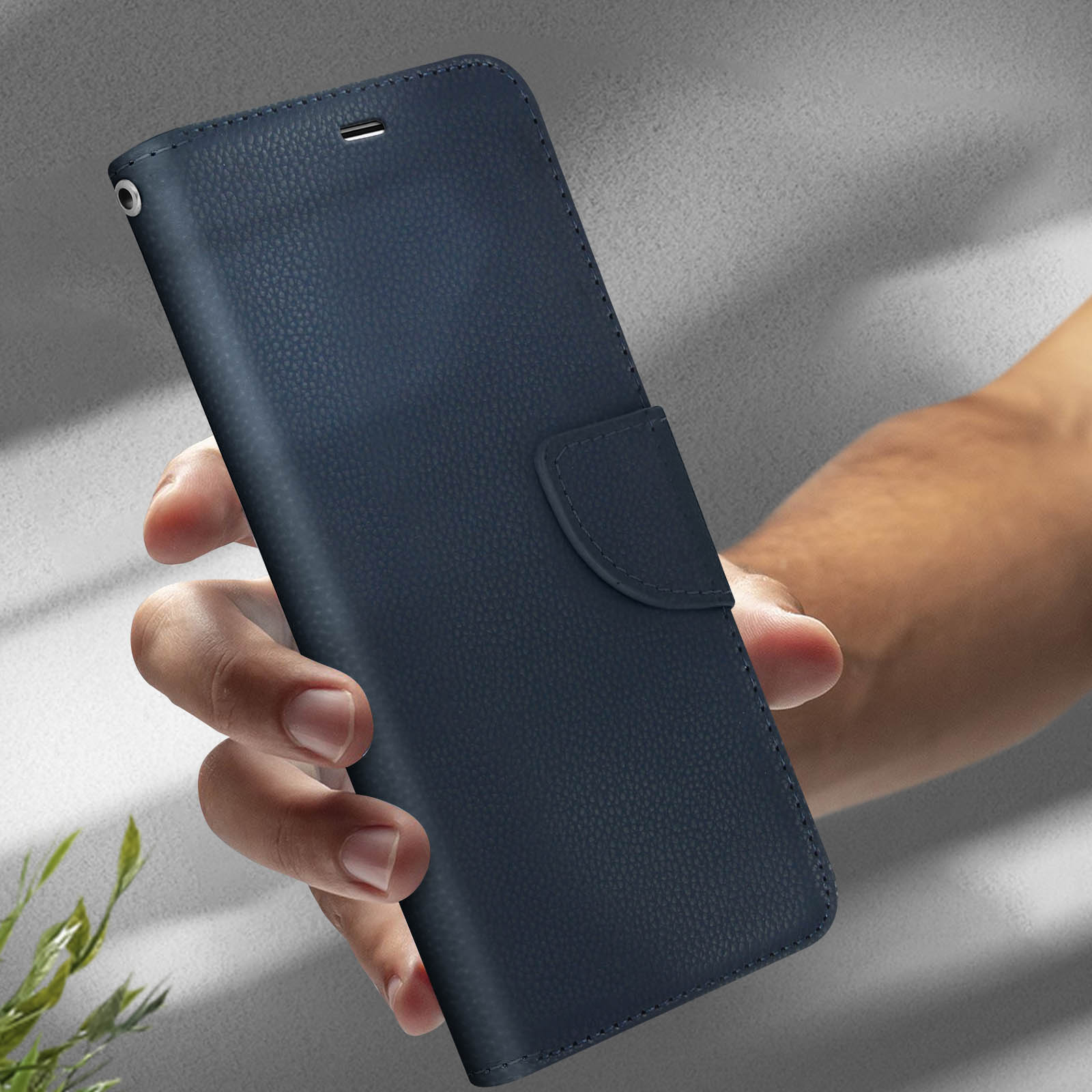 Mano che tiene una custodia per telefono in pelle blu. Sfondo grigio. La custodia è chiusa.