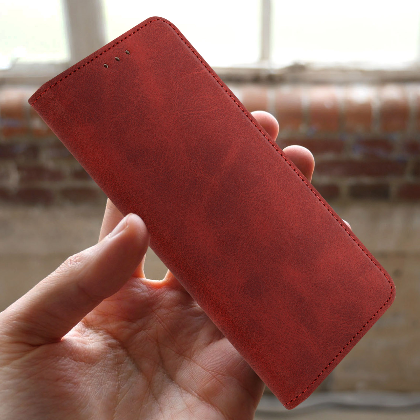 Mano che tiene una custodia per telefono in pelle rossa. La custodia è chiusa, con cuciture visibili.