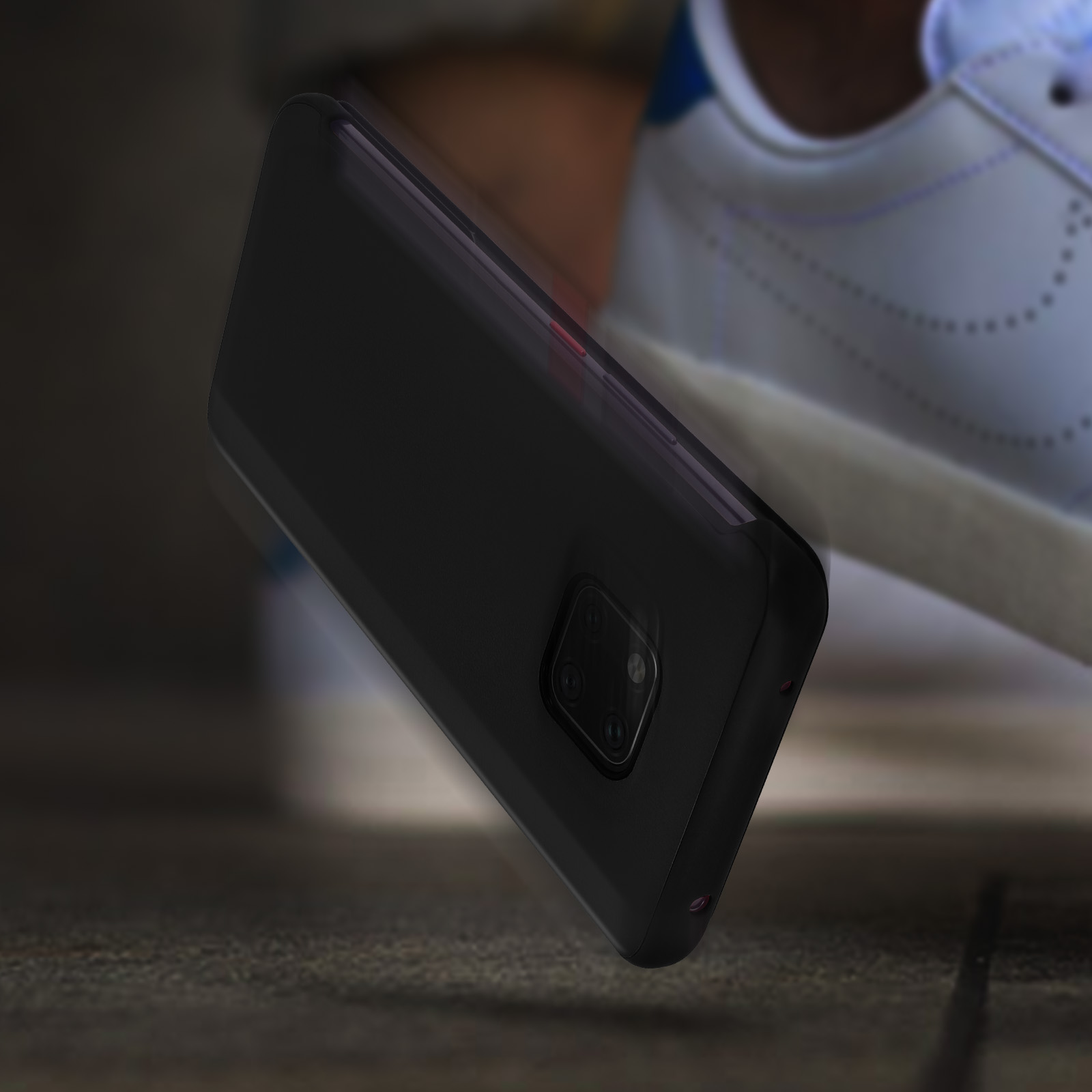 Un telefono nero sta cadendo, vicino a una scarpa da ginnastica. Il telefono ha un obiettivo. Il pavimento è di legno.