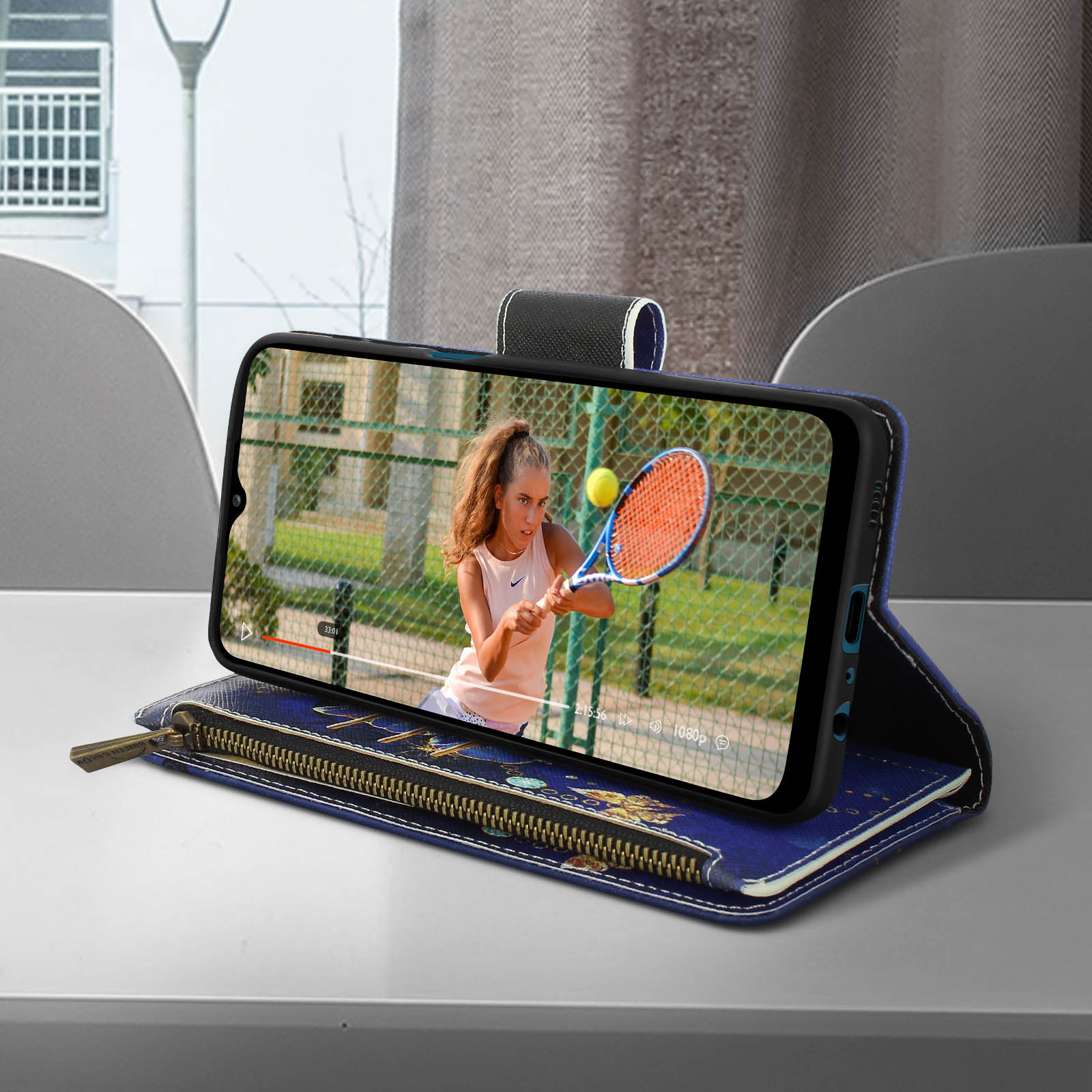 Ein Telefon zeigt ein Tennisvideo. Das Telefon ist in einer blauen Geldbörsenhülle auf einem Tisch.
