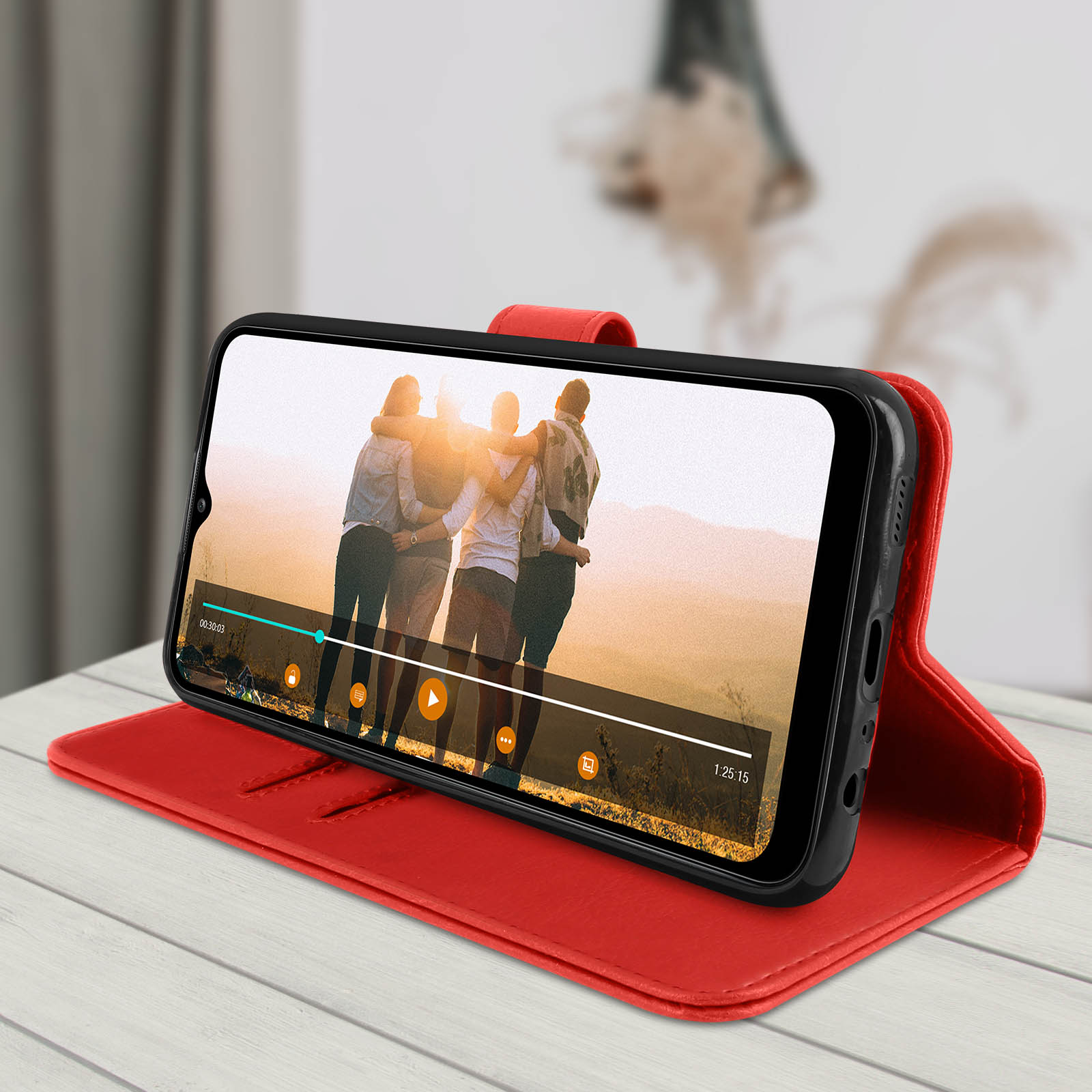 Un telefono in una custodia di pelle rossa è aperto su una superficie di legno. Un video è in riproduzione sullo schermo.