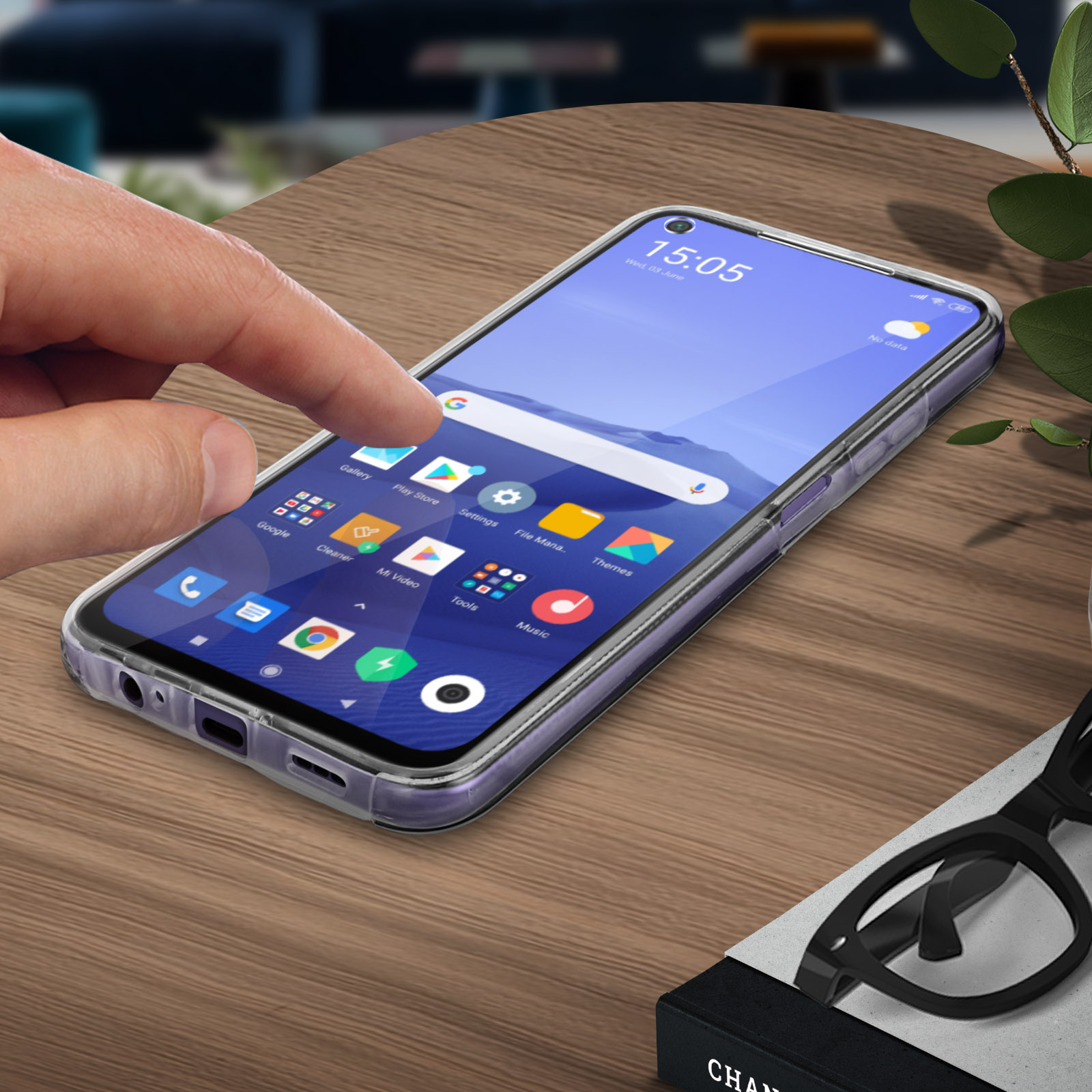 La main touche l'écran d'un téléphone. Le téléphone est dans un étui transparent sur une table en bois.