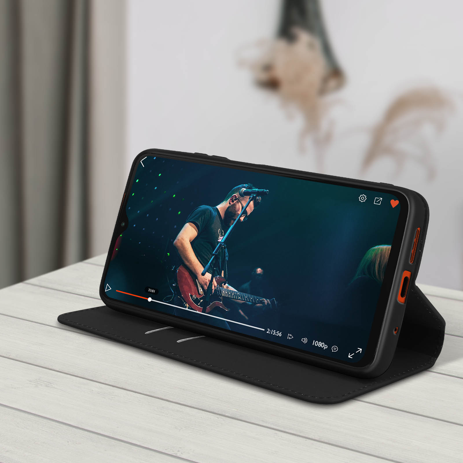 Téléphone sur un support montrant une vidéo d'un homme jouant de la guitare. Le support est sur une table en bois.