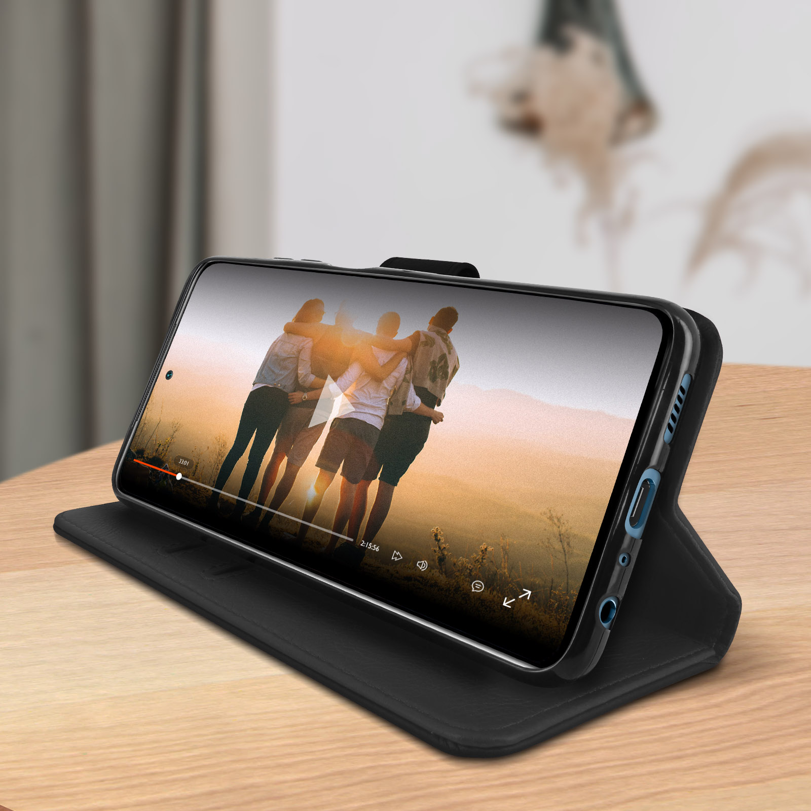 Een telefoon in een zwarte hoes geeft een video weer. Hij ligt op een houten tafel.