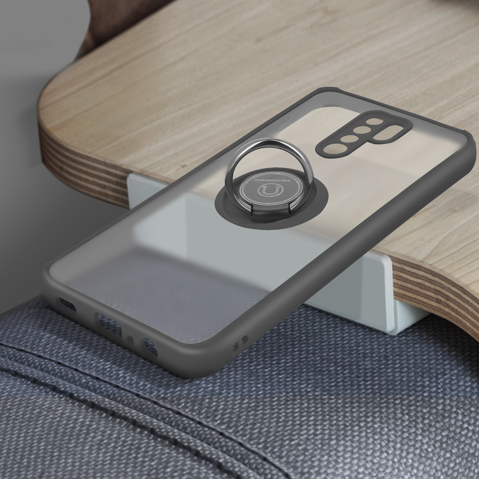 Un telefono in una custodia trasparente con un supporto ad anello. Poggia su uno scaffale di legno. Sotto ci sono jeans grigi.