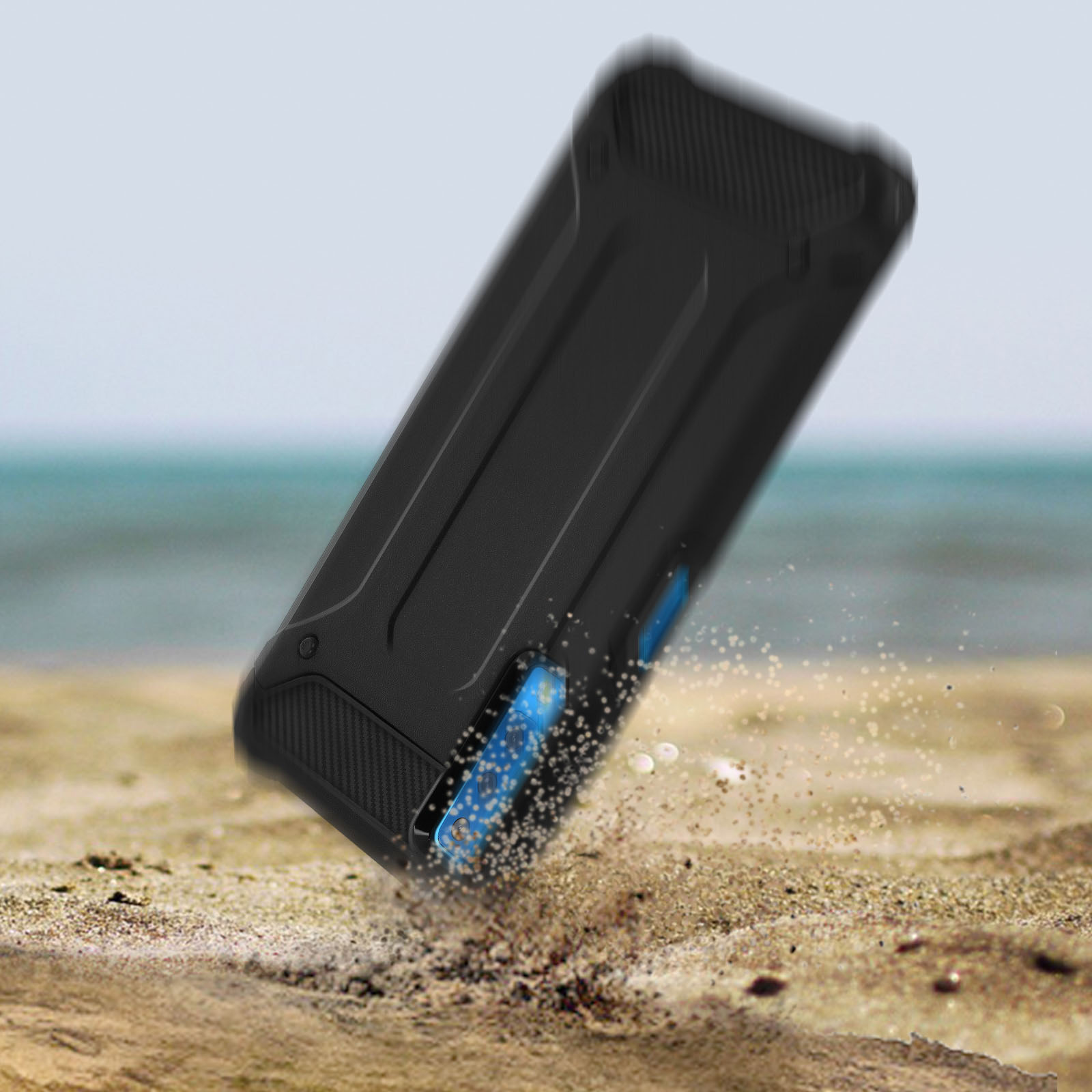 Eine schwarze Handyhülle liegt im Sand, Sand fliegt. Der Hintergrund ist das Meer.