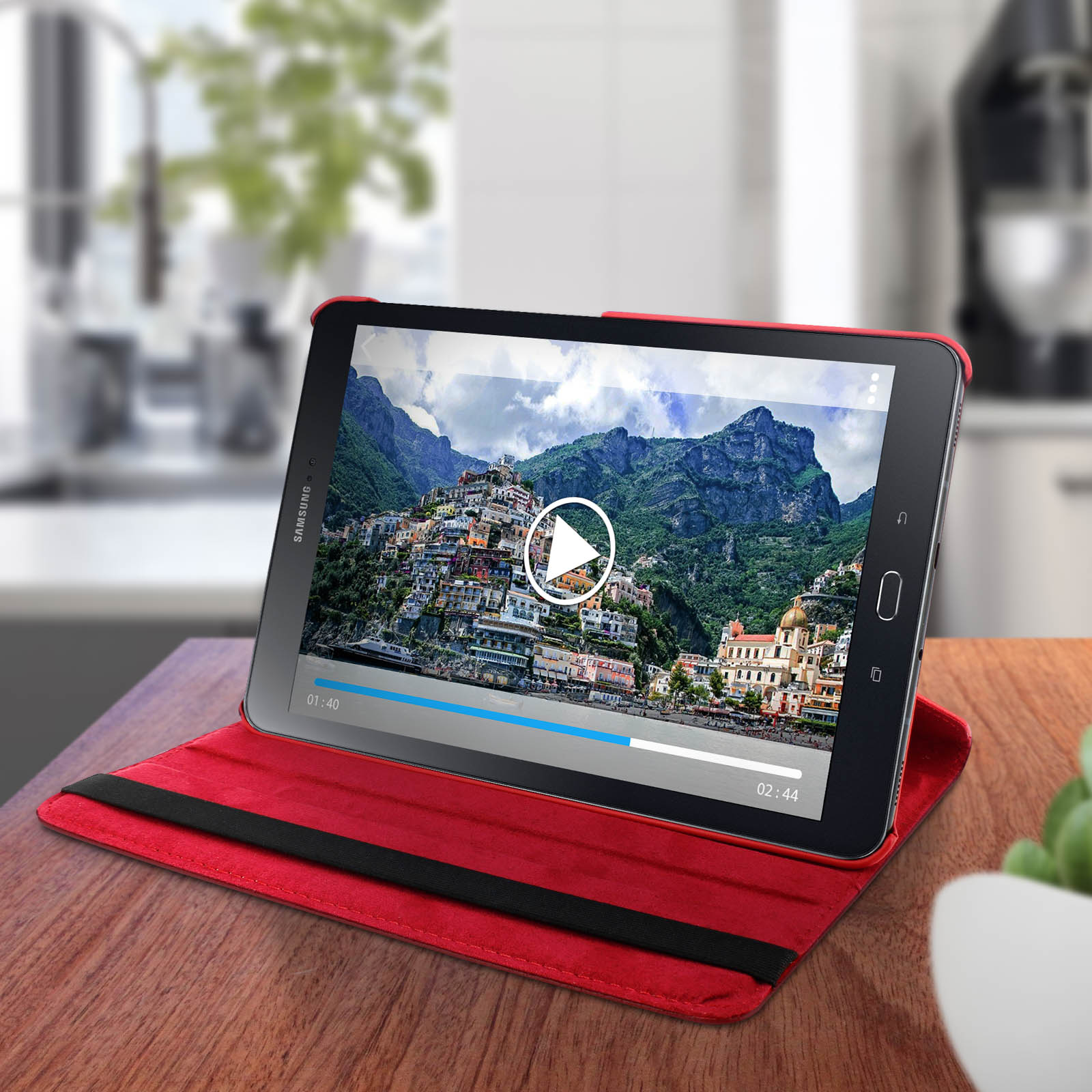 Il tablet mostra un video di una città costiera. Il tablet è in una custodia rossa ed è su un tavolo di legno.