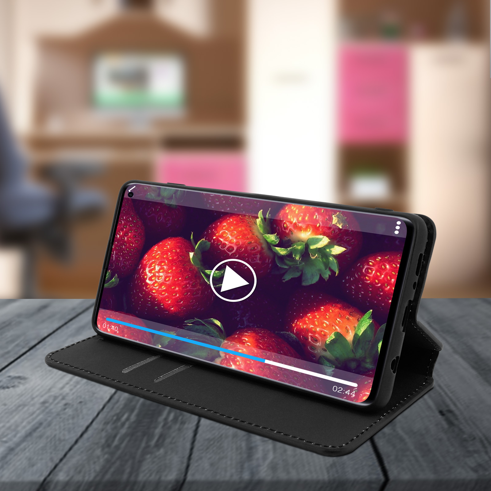Smartphone che mostra un video di fragole in una custodia. Custodia aperta su un tavolo di legno.