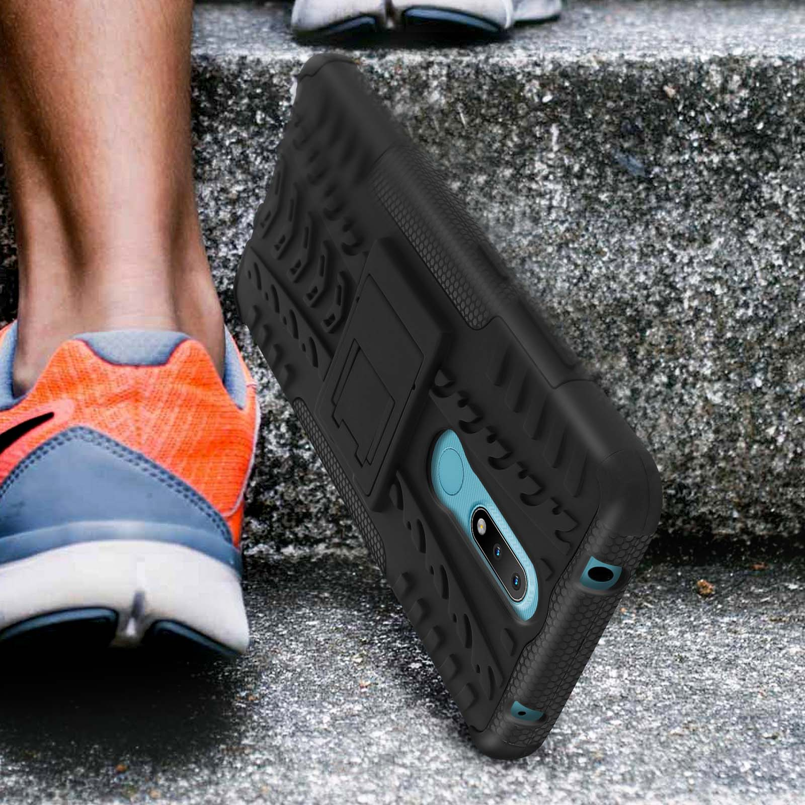 Custodia nera e robusta per telefono con cavalletto, accanto alle gambe e alle scarpe di una persona.
