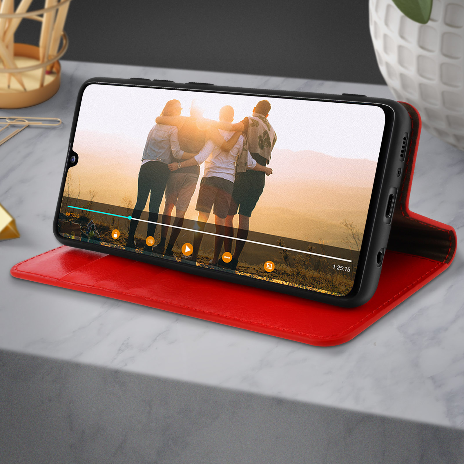 Un téléphone dans un étui rouge, lisant une vidéo. Il est sur une surface rouge à motif marbre.