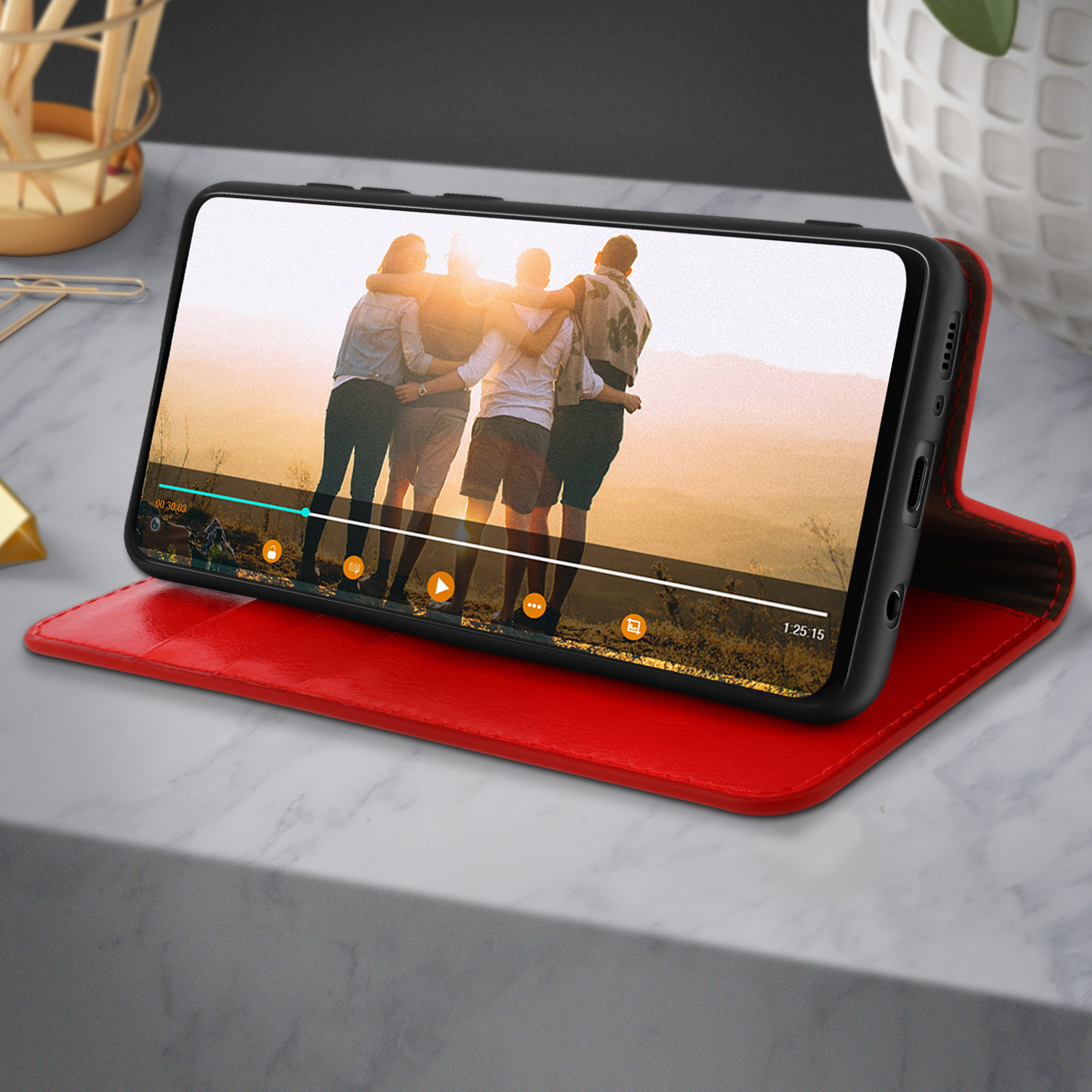 Téléphone sur étui rouge affichant une vidéo avec des personnes. Placé sur une surface en marbre.