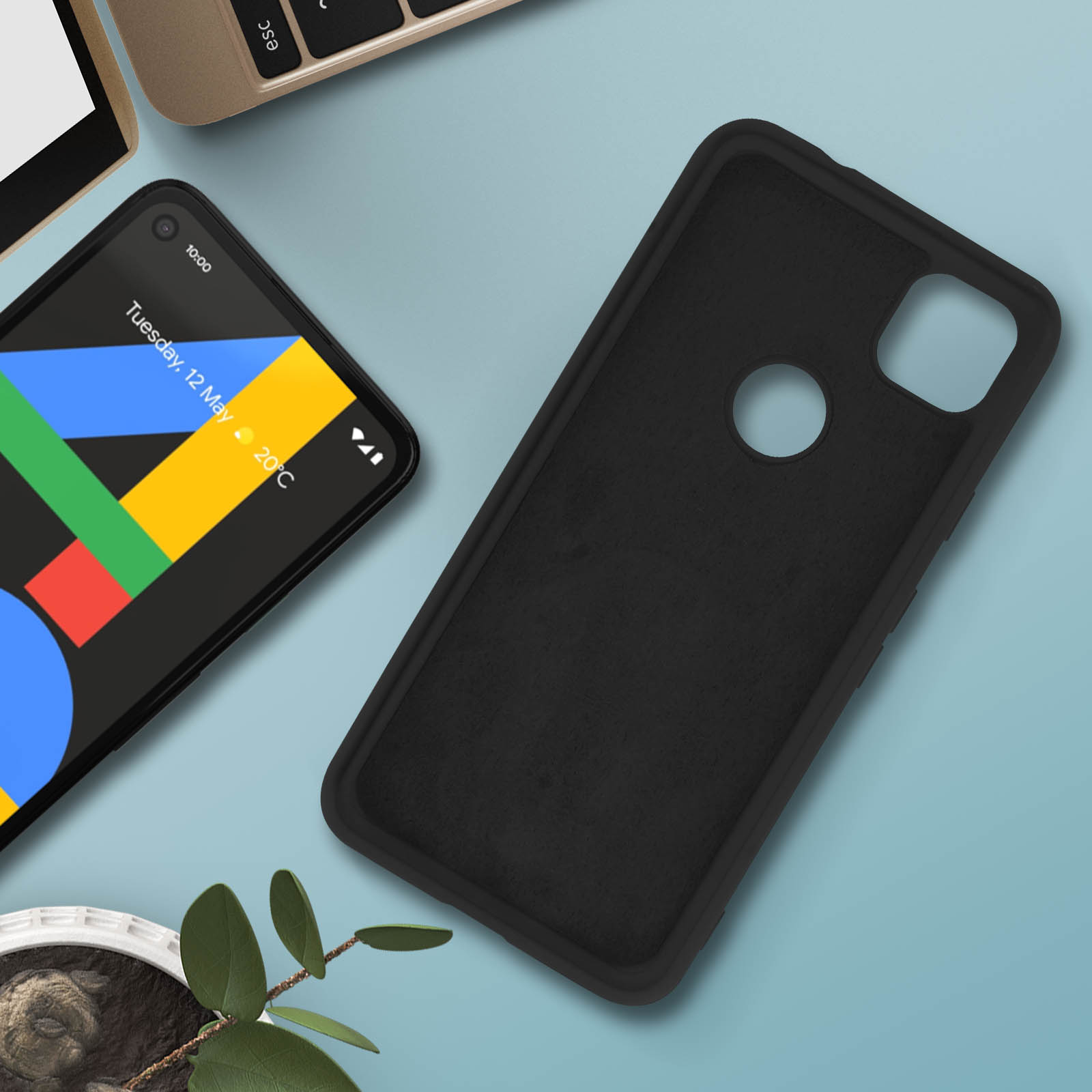 Un téléphone avec un étui noir posé sur une surface bleue, avec plante et ordinateur portable.