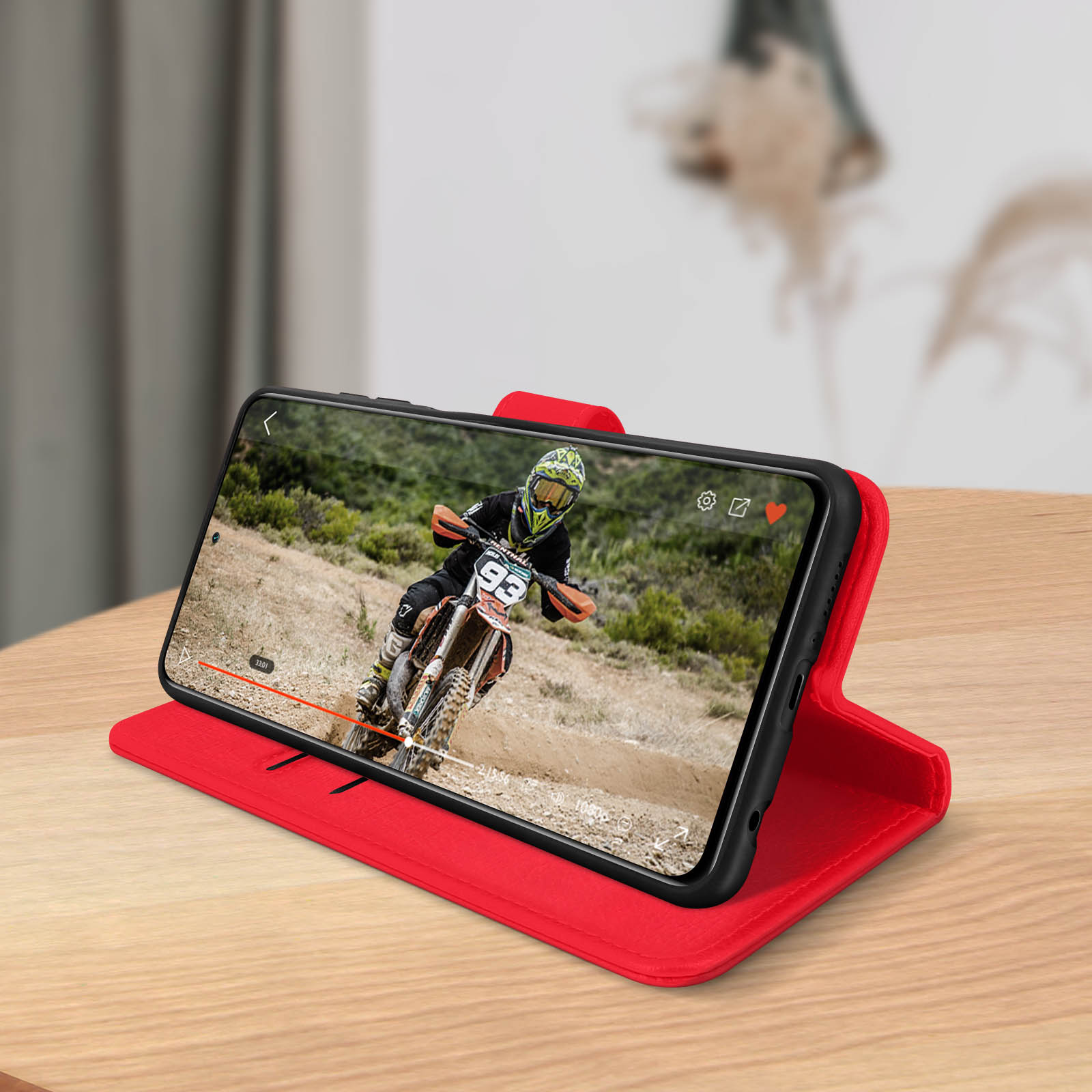 Telefono in custodia rossa che mostra video di motocross. Sfondo tavolo in legno.