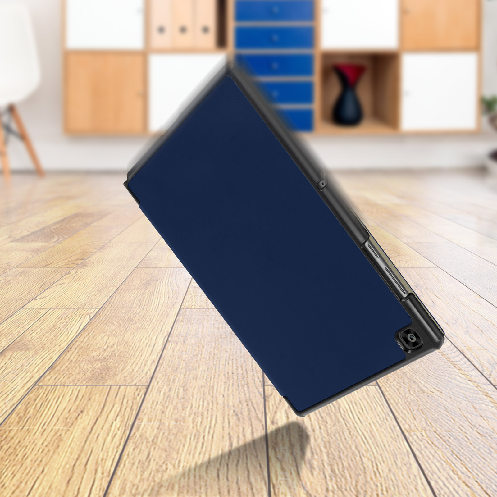 Custodia blu per tablet che cade. Sfondo pavimento in legno. Oggetti sfocati. Custodia blu scuro.