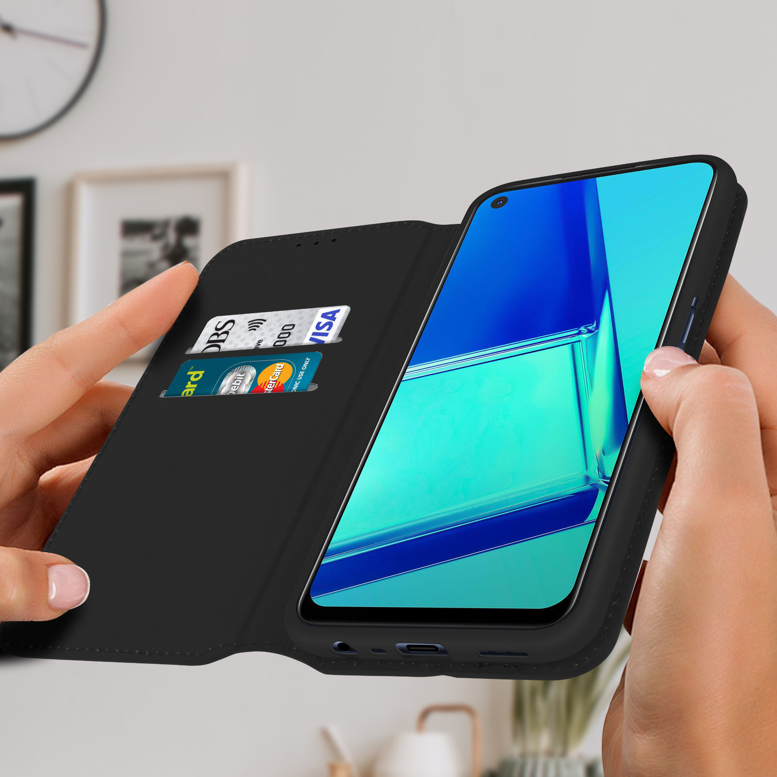 Une personne tenant un téléphone dans un étui noir, avec des cartes de crédit. Le fond est une pièce.