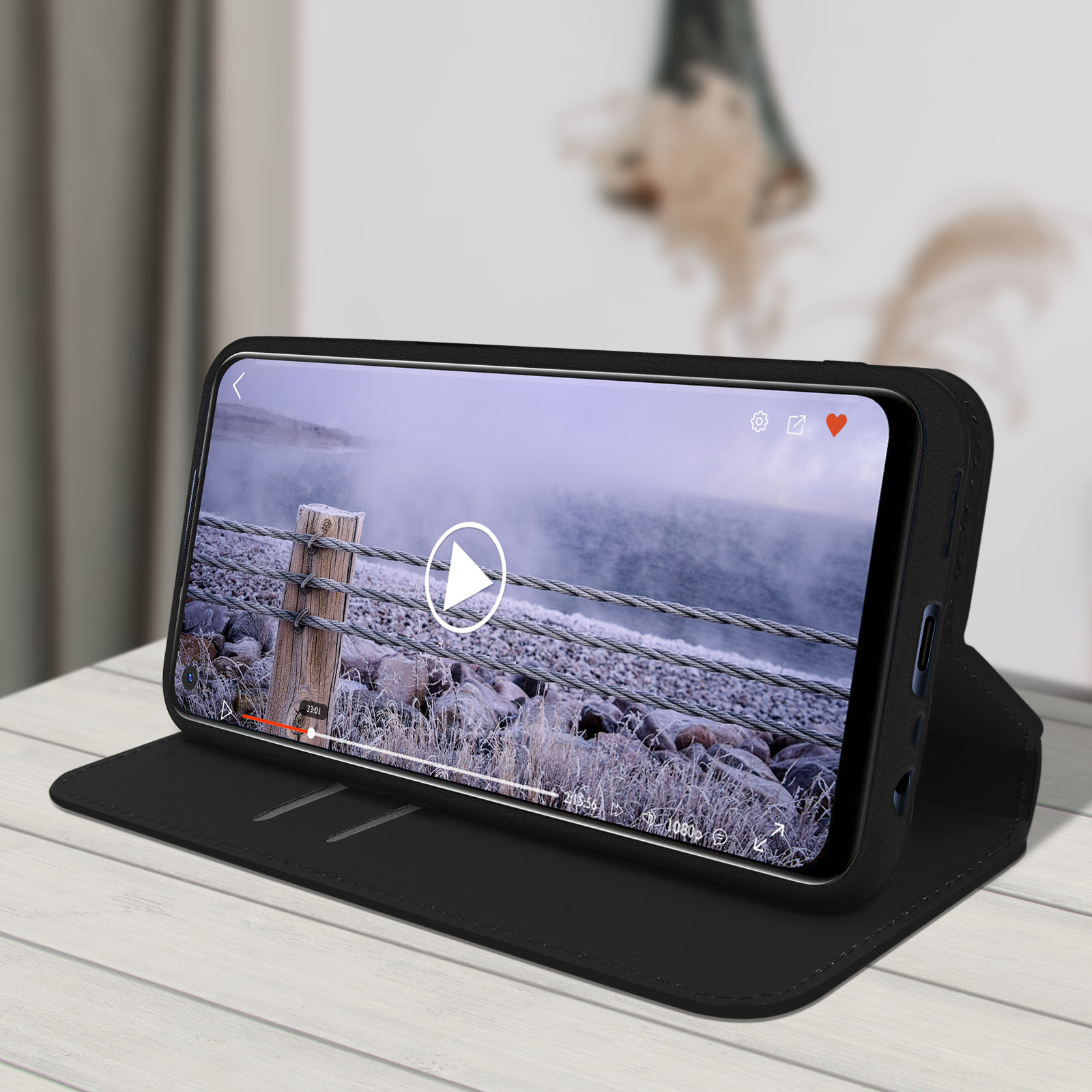 Coque de téléphone noire avec un téléphone à l'intérieur. L'écran affiche une vidéo. La coque est ouverte sur une table en bois.