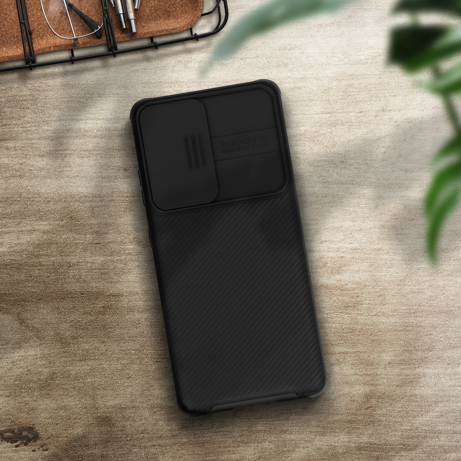 Una custodia nera per telefono con una copertura scorrevole per la fotocamera. La custodia è su una superficie di legno con alcuni oggetti.